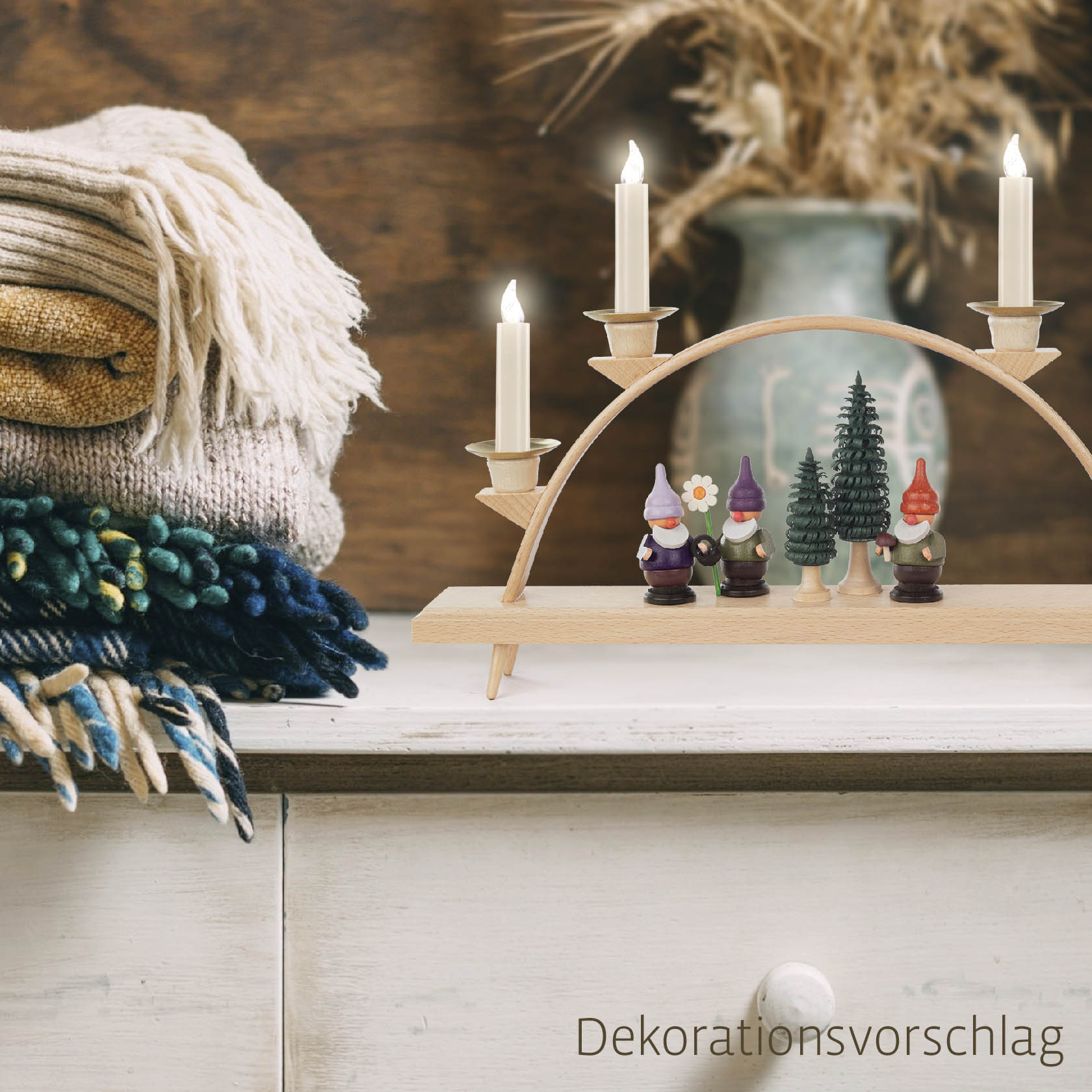 A large unassembled arched candle holder for four pyramid candles, featuring gnome figurines and a small tree, placed on a wooden table.