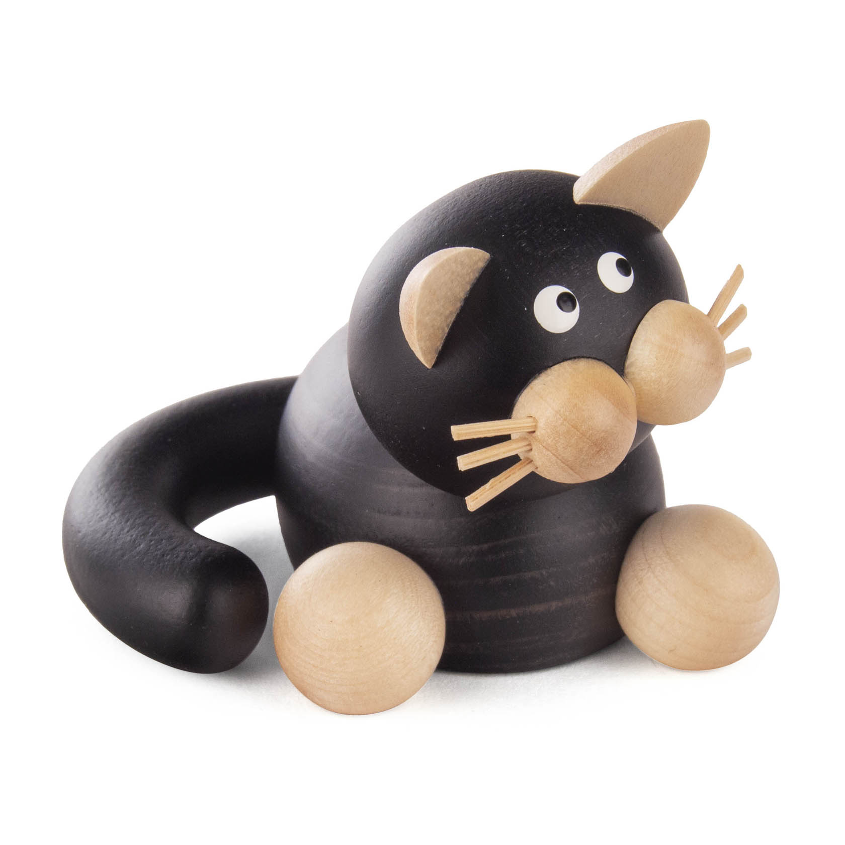 A small wooden black and white cat figurine with exaggerated features, including large round eyes and a curled tail, sitting on its haunches.