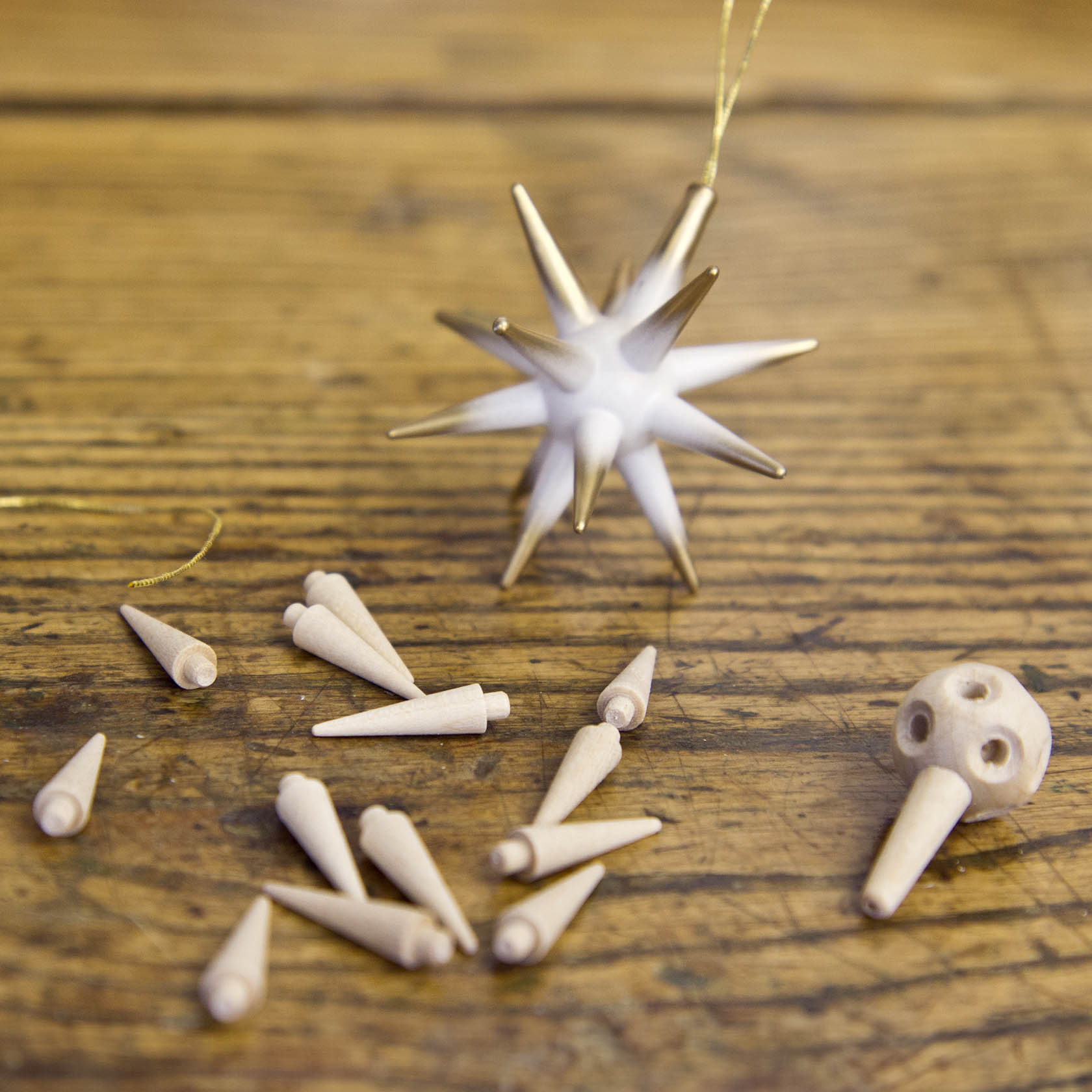 Ein Christbaumschmuck in Form eines weißen Sterns mit goldenen Spitzen liegt auf einem Holztisch. Daneben liegen Einzelteile dieses Sterns.