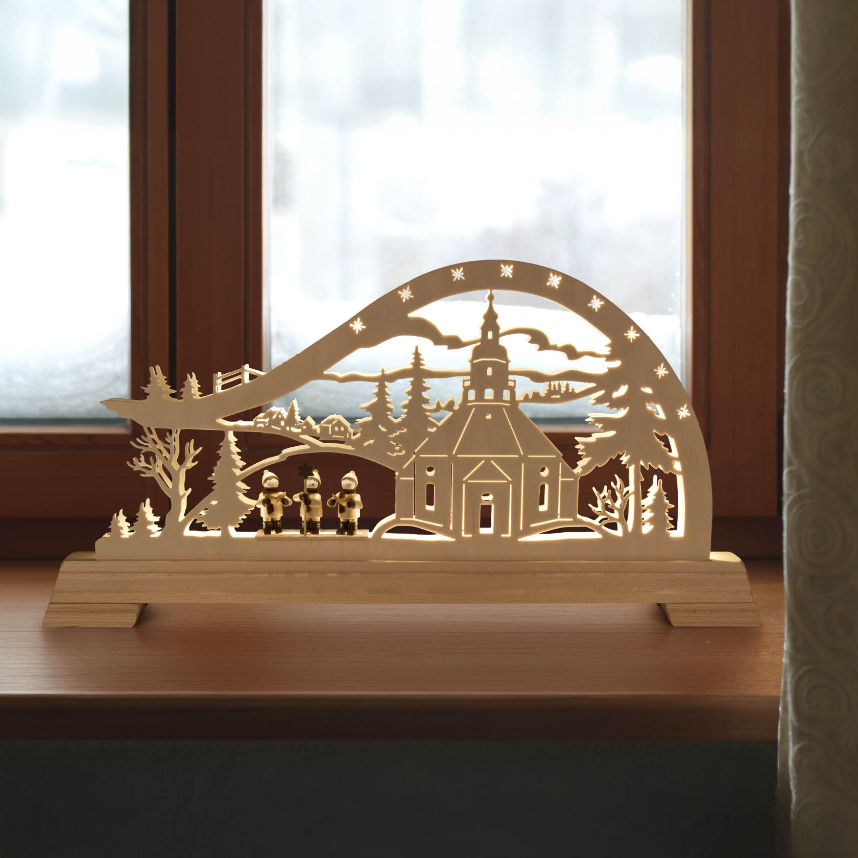Holz-Schwibbogen mit Seiffener Kirche und Kurrende-Sängern, festlich beleuchtet mit LED-Lichtern, auf einem Fenstersims platziert.