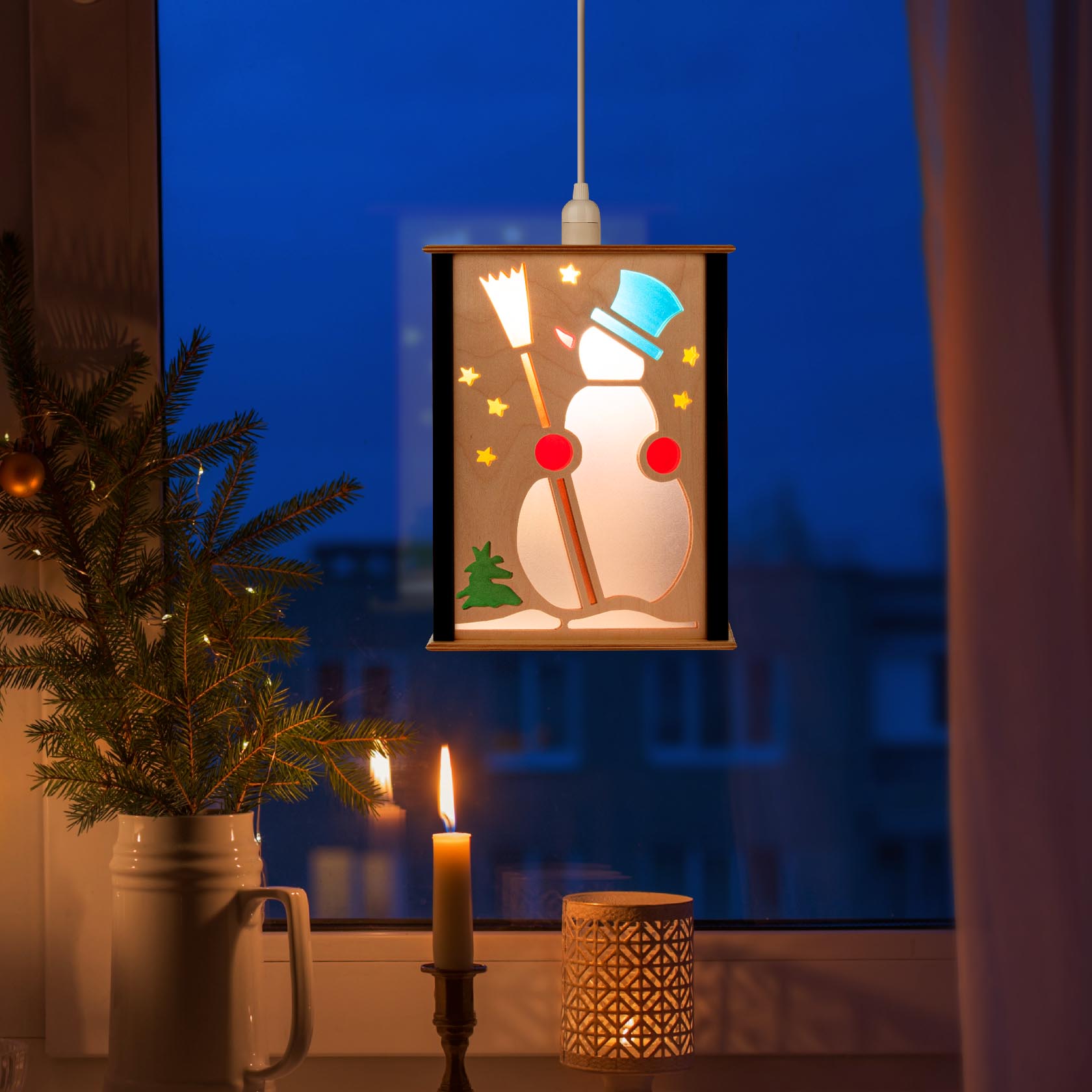 Fensterlaterne mit Nussknacker-Dekor: ein Schneemann mit blauem Zylinder und rotem Schal, umgeben von gelben Sternen, erleuchtet von innen.