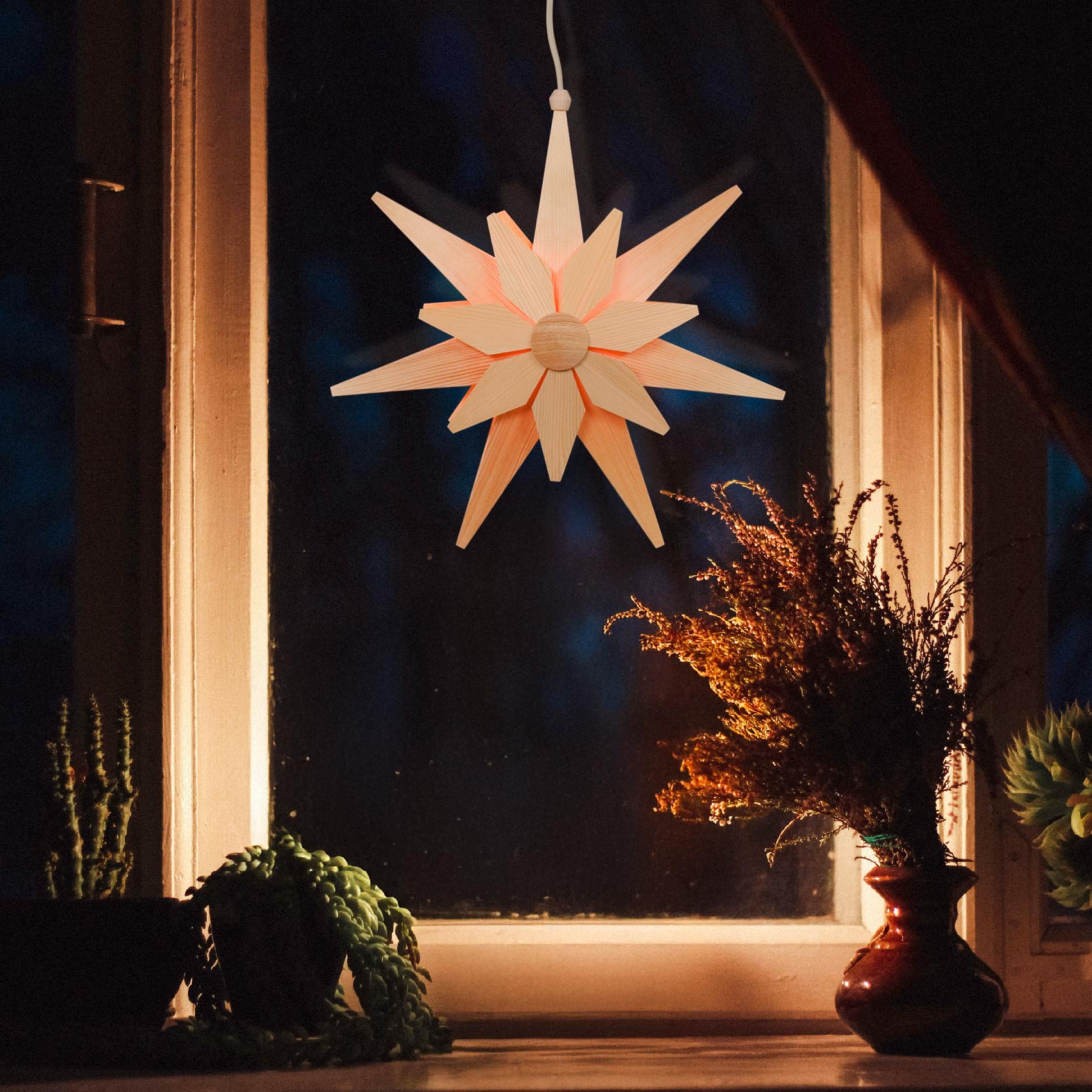 A double-layered natural wooden star with electric lighting hanging in a window, creating a warm, cozy ambiance inside a room.