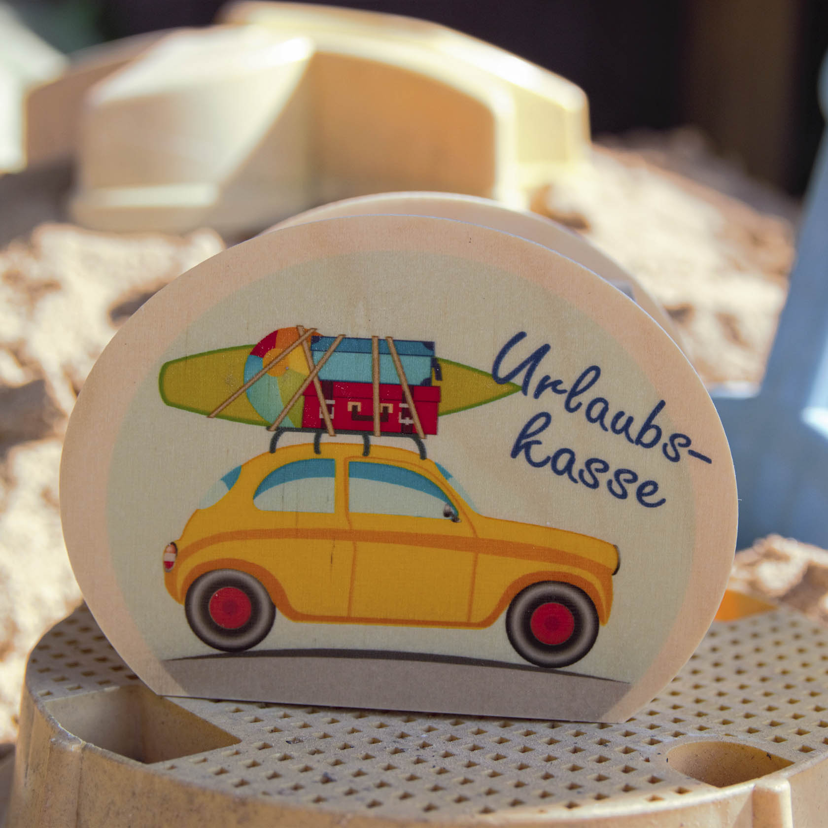 A piggy bank with a retro yellow car illustration carrying luggage and a surfboard, with the text 'Urlaubskasse' printed on it.