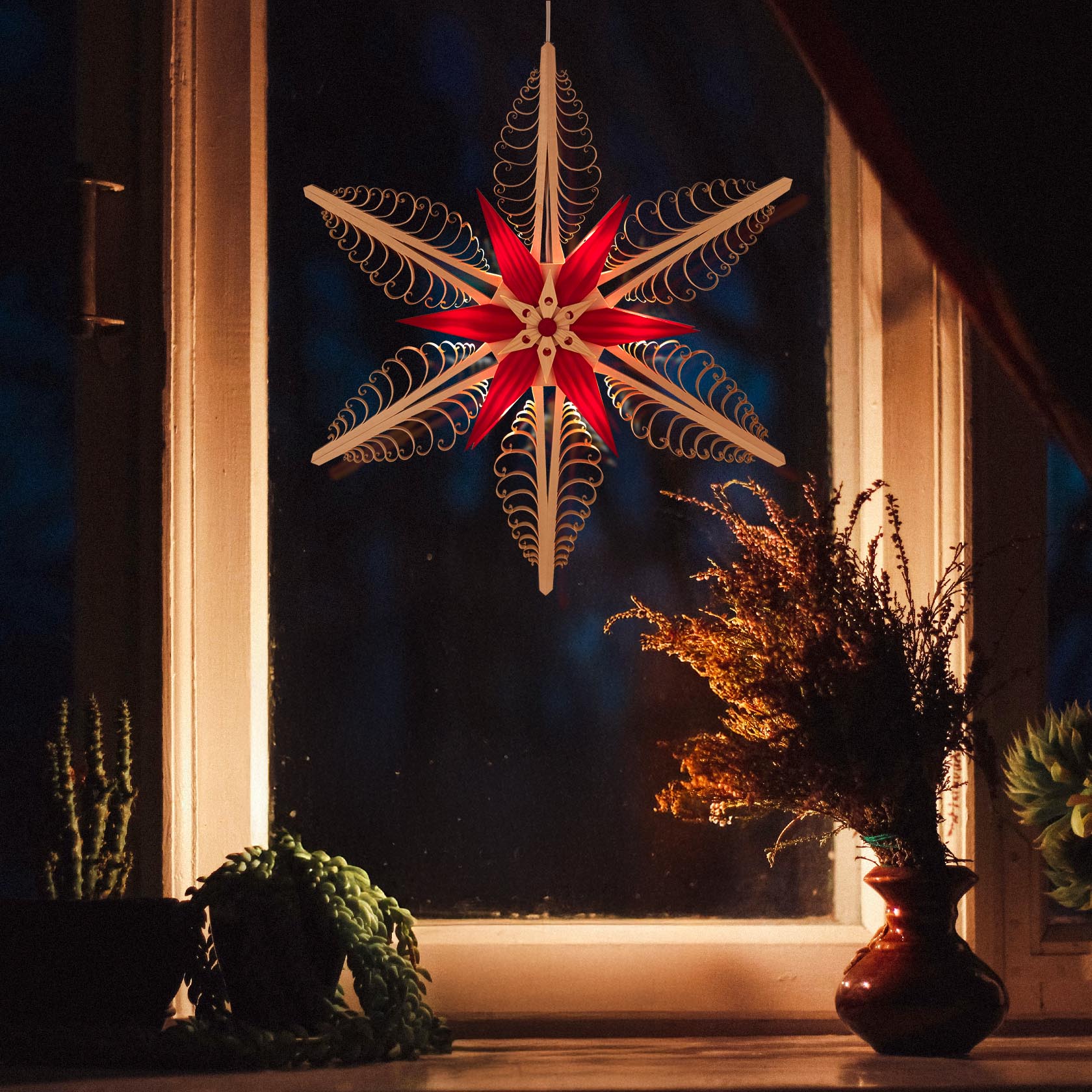 A natural-red wooden Span star with electric lighting hangs in a window, casting a warm glow. Plants and a vase are visible on the windowsill.