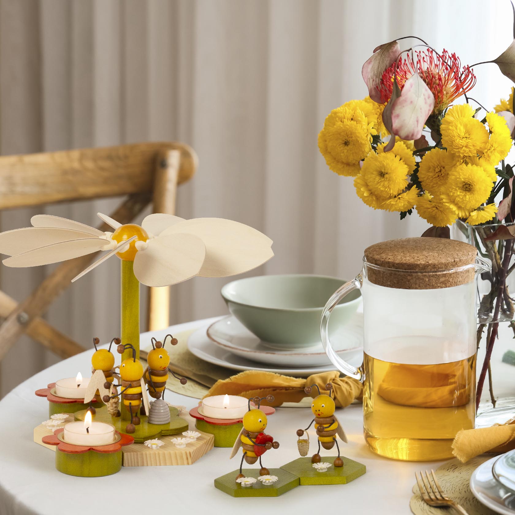 Holzpyramide mit Bienenfiguren, Teelichtern, drei Kerzenhaltern und einer großen Blume oben als Flügel auf einem gedeckten Tisch.
