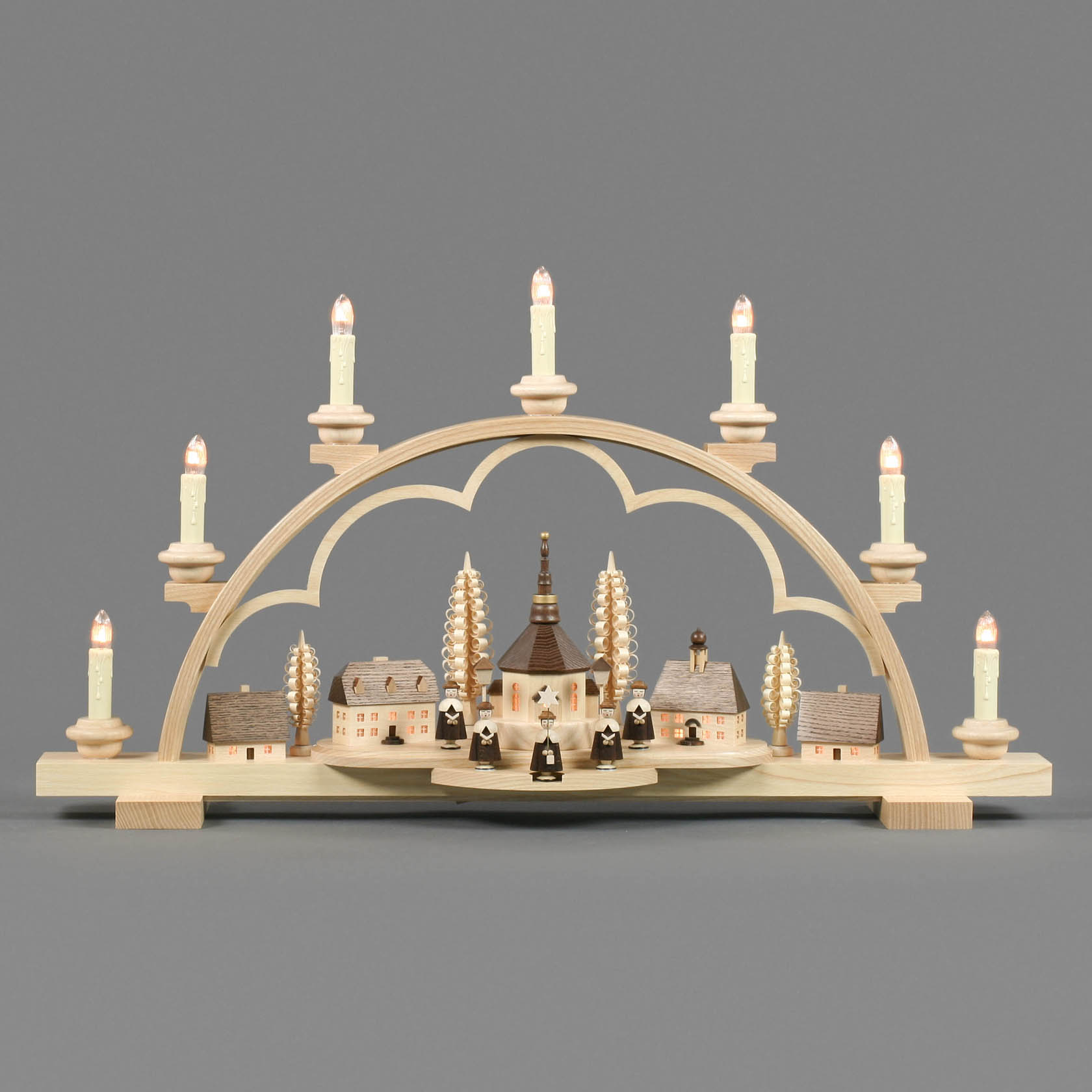 Wooden arch with electric candles depicting Seiffen village. Central church scene with figures and buildings, all illuminated from within.