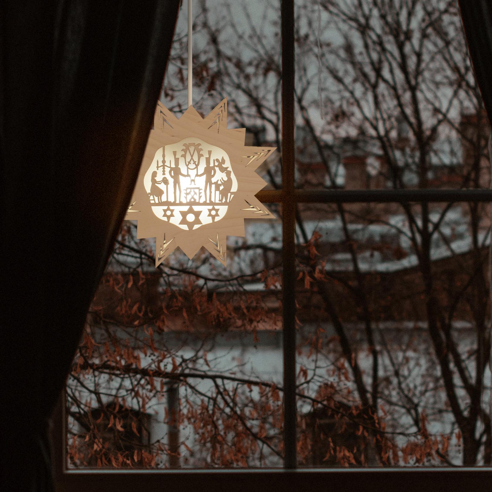 Ein beleuchteter Weihnachtsschmuck in Sternform aus Papier hängt vor einem Fenster. Das Design zeigt weihnachtliche Motive, die durch elektrisches Licht betont werden.