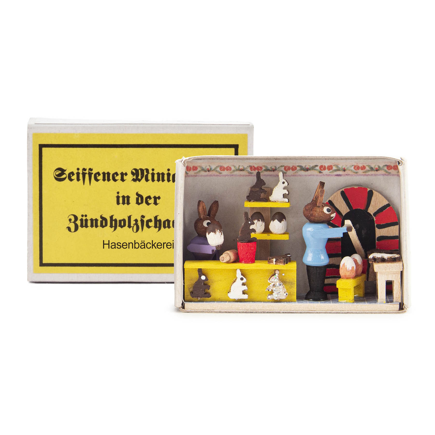A miniature bakery scene with rabbit figurines inside a matchbox, showing a baker rabbit in blue with other rabbit figures and bakery items. im Dregeno Online Shop günstig kaufen