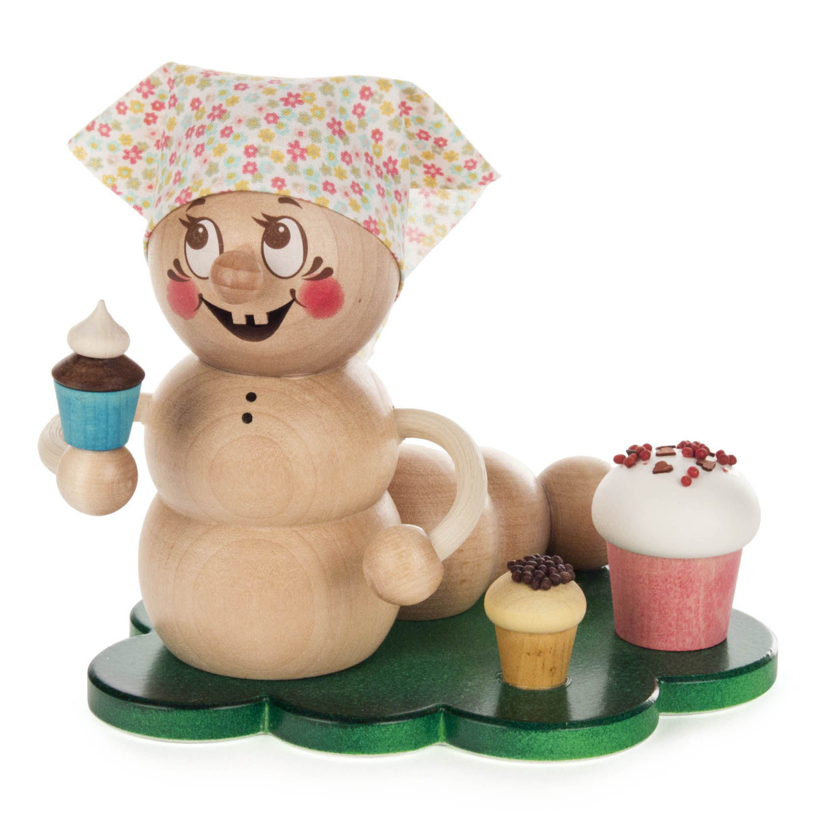 Holzfigur Räucherwurm Rosi mit pinken Wangen, großer Nase, Blumenmütze, hält blauen Cupcake in der Hand, zwei weitere Cupcakes auf grünem Untergrund. im Dregeno Online Shop günstig kaufen