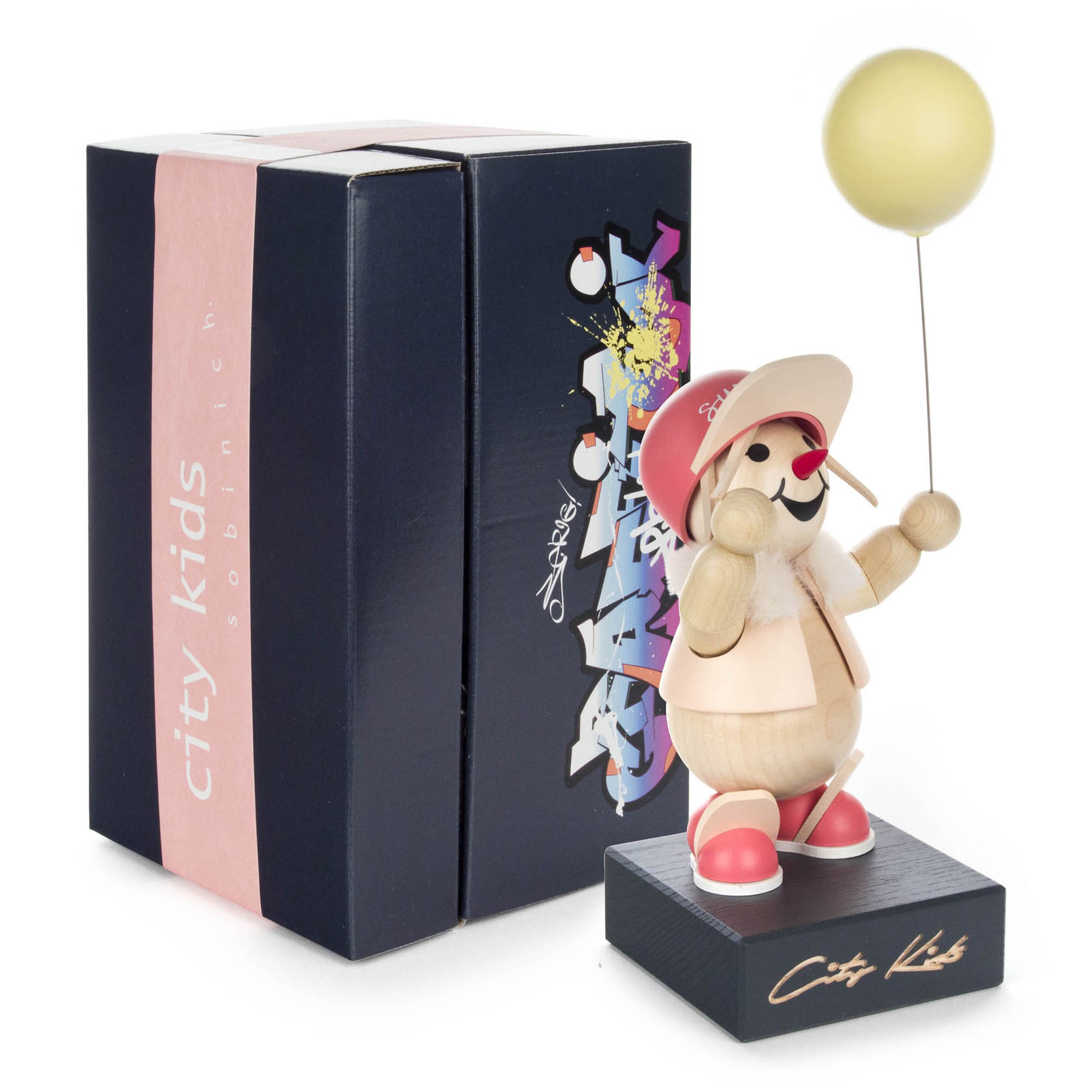 A wooden figurine named 'Abbie' from the 'City Kids' collection, wearing a pink hat, holding a yellow balloon, and standing on a black base.