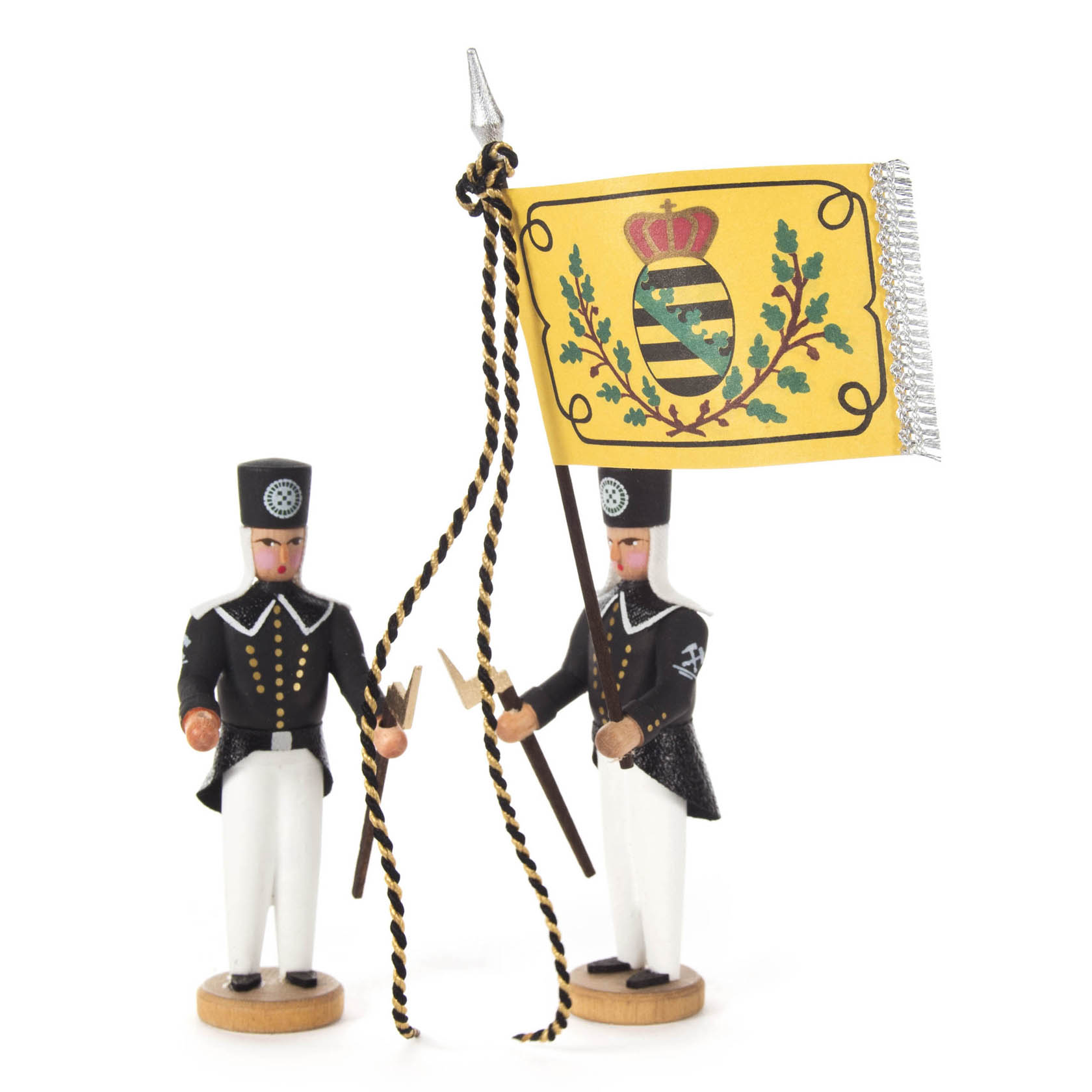 Two small wooden figurines dressed in traditional uniforms, one holding a yellow flag with a coat of arms and the other with a staff.