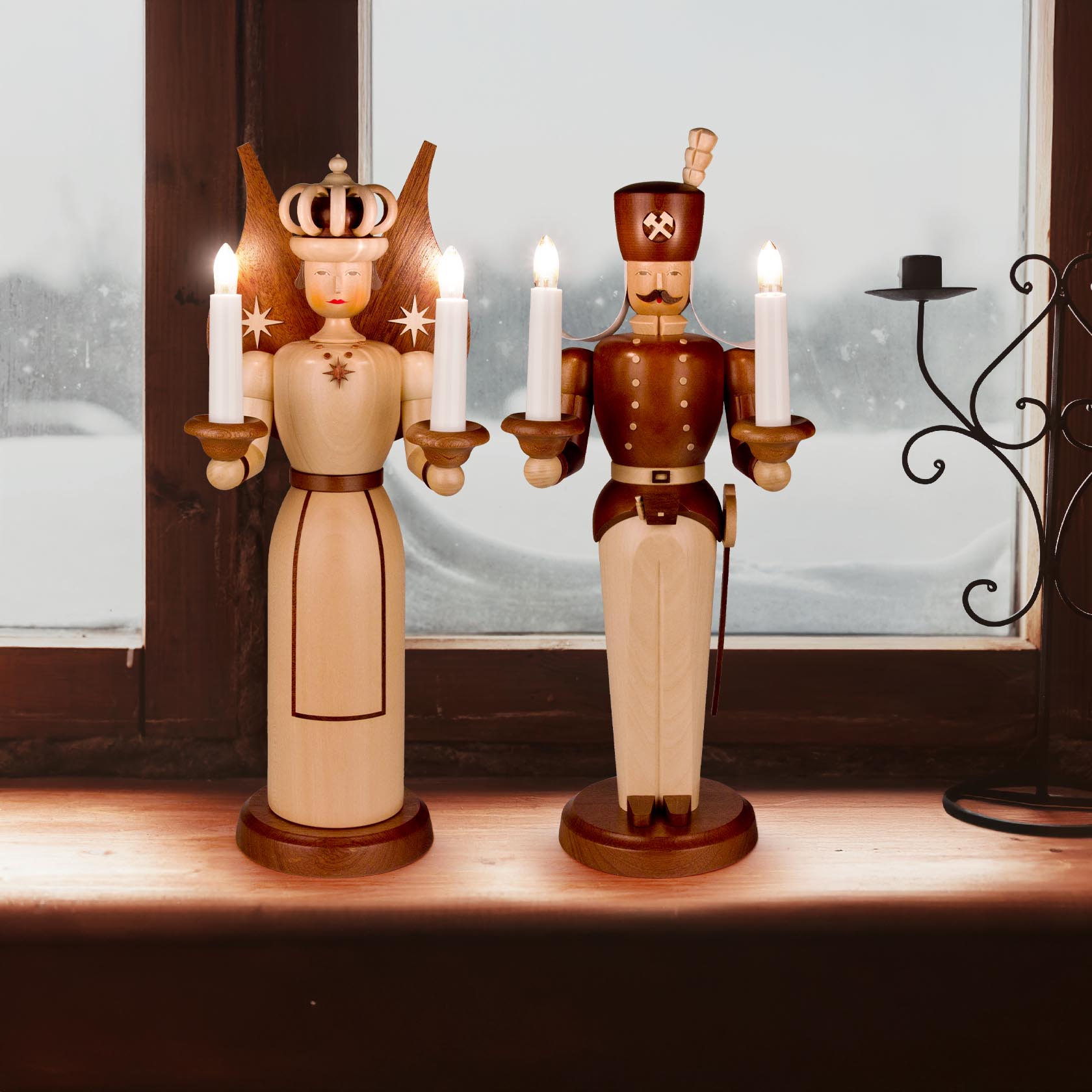 Zwei elektrisch beleuchtete Holzfiguren, Engel und Bergmann, jeweils 40 cm hoch. Sie halten Kerzenhalter mit Kerzen und stehen auf einem Fensterbrett.