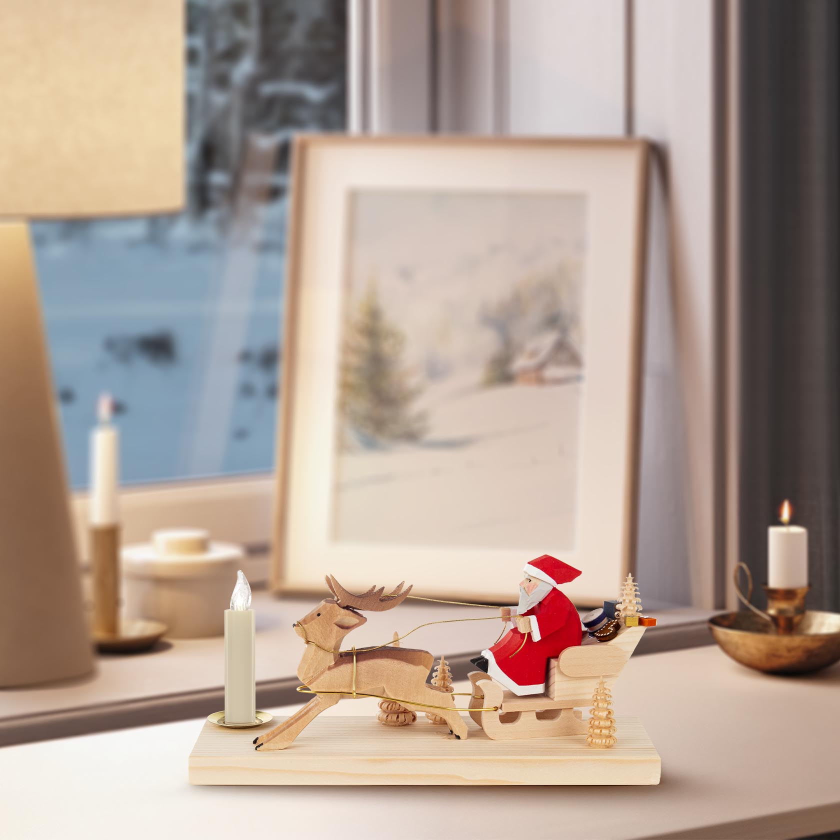 Holzfiguren des Weihnachtsmanns im roten Anzug, der in einem von einem Rentier gezogenen Schlitten sitzt. Links davon eine Kerze auf einem Holzsockel.