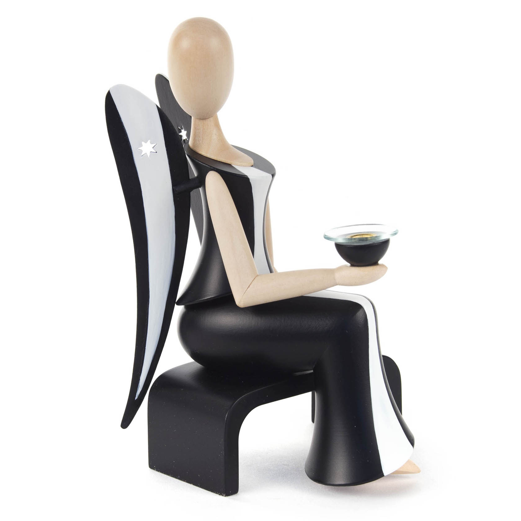 A wooden angel figurine, 15.5cm tall, with black and white wing design, seated and holding a candle holder. The wings have star-shaped cutouts.