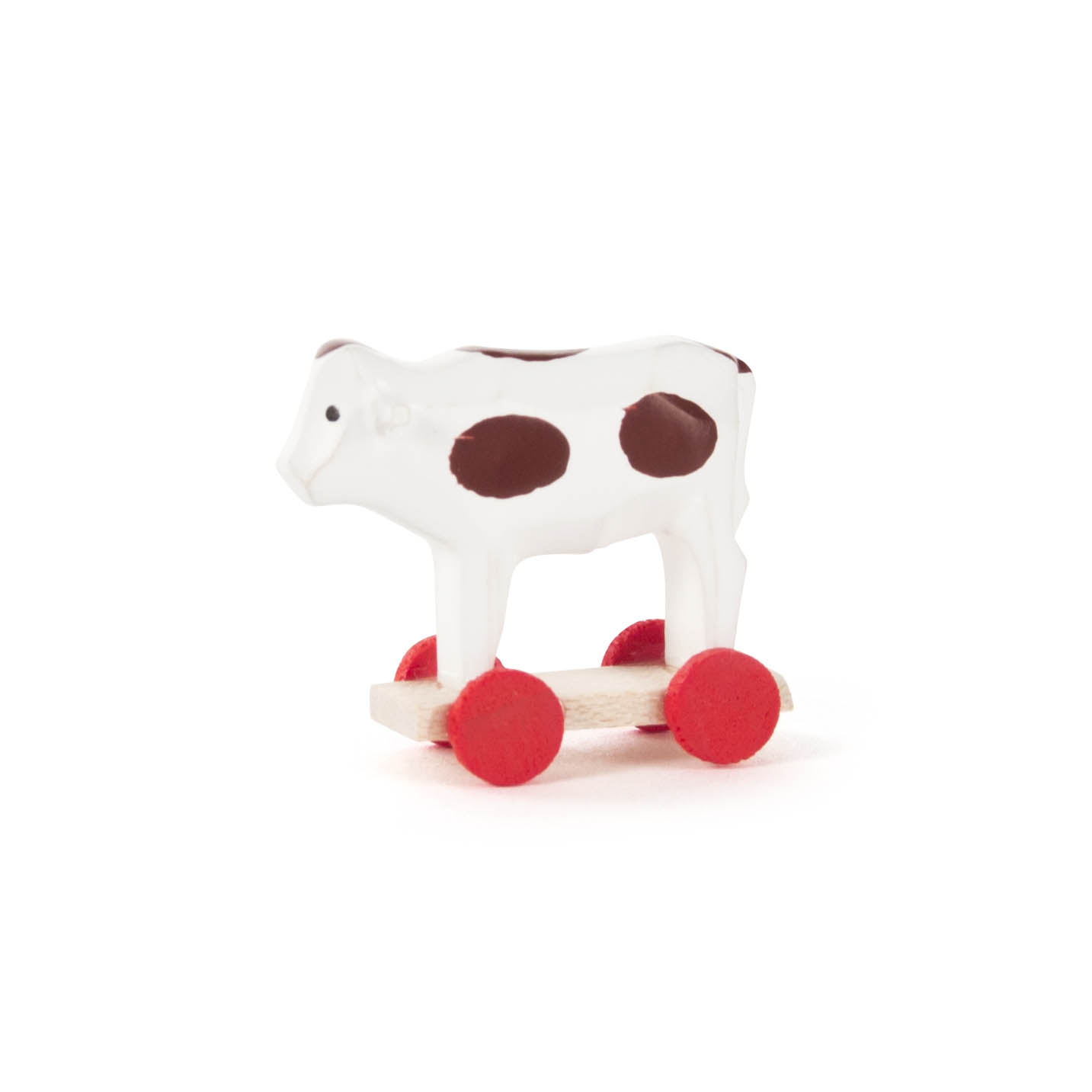 A small white toy cow with brown spots mounted on red wheels.