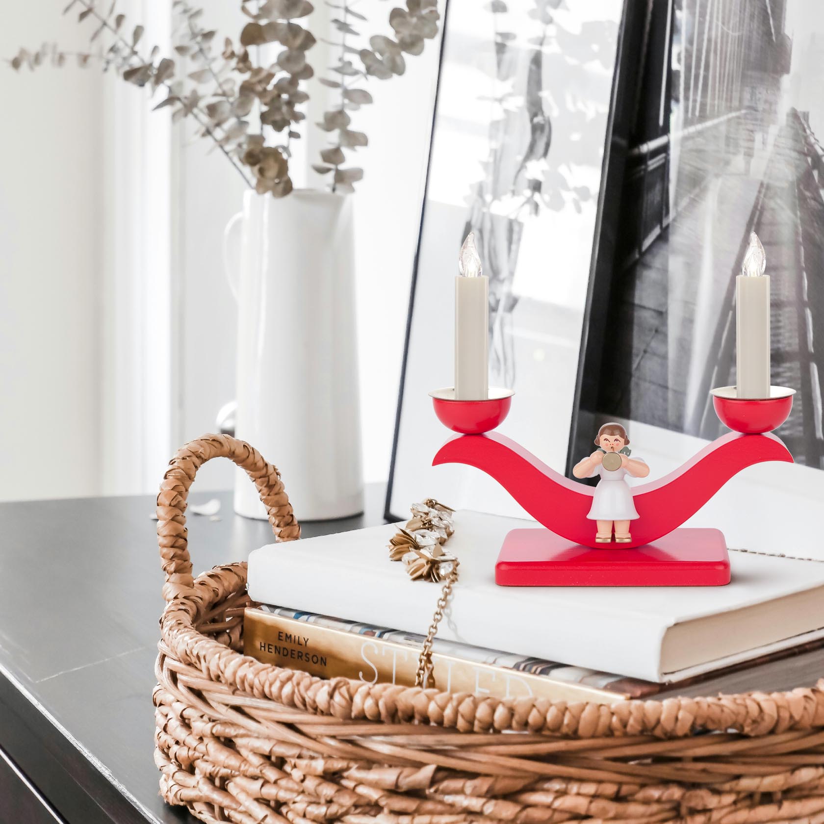 A colorful candle holder featuring an angel in white robe, holding two candle sockets designed for 14mm candles, placed on a red curved base.