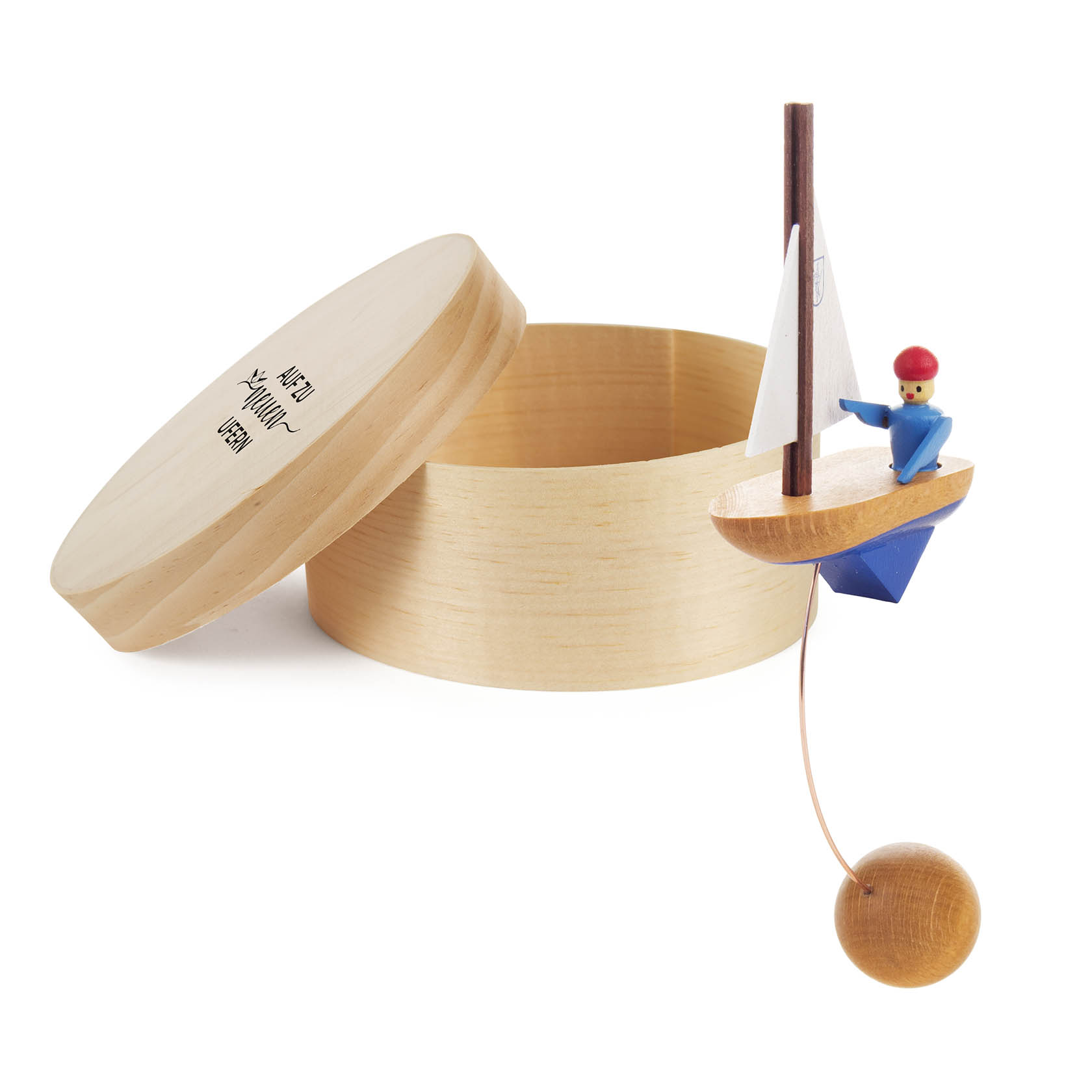 Wooden toy sailboat with a sailor, balanced on a string with a wooden ball, presented in an open cylindrical wooden box.
