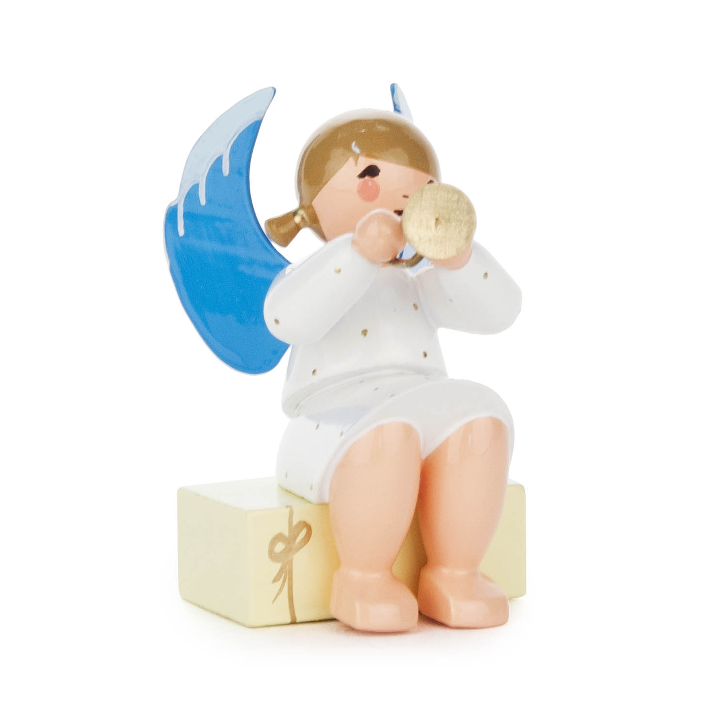 A small angel figurine with blue wings, wearing a white robe with gold dots, sitting on a gift box while playing a golden trumpet.