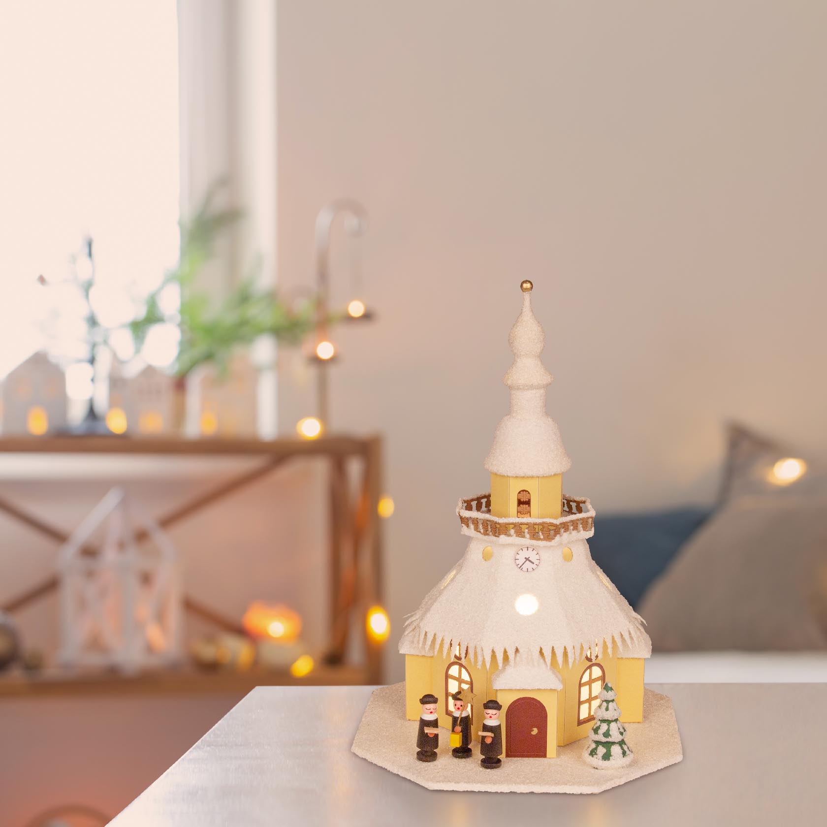 Wooden model of Seiffen Church with electric lighting, snow-covered roof, featuring three figures and a small Christmas tree.