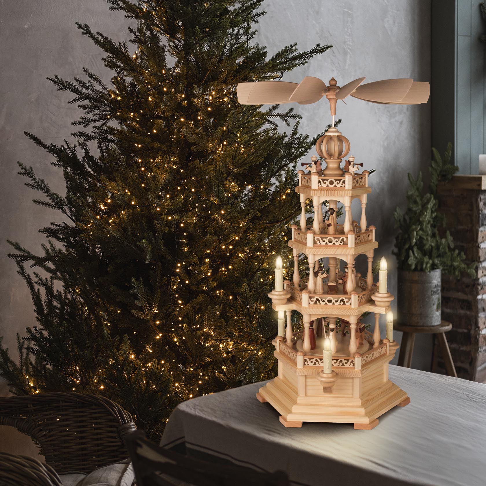 Eine dreistöckige Weihnachtspyramide mit der Szene der Geburt Christi, elektrisch beleuchtet und angetrieben. Sanft beleuchteter Weihnachtsbaum im Hintergrund.