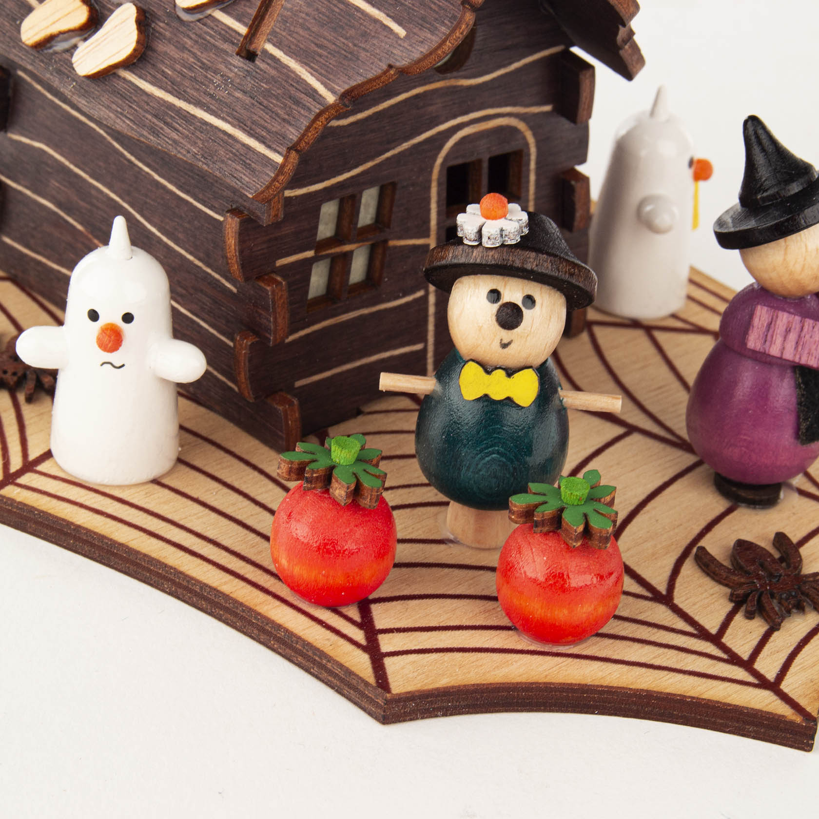 A wooden incense burner shaped like a Halloween-themed house with two figures: a witch and a ghost. Two small pumpkins are in the foreground.