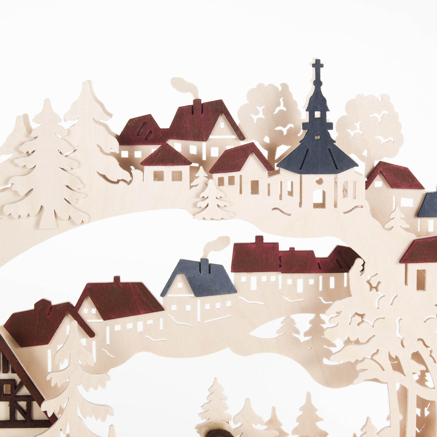 A small, intricately designed arch-shaped candle holder 'Schwibbogen', depicting a winter village scene with a church and houses, electrically lit.