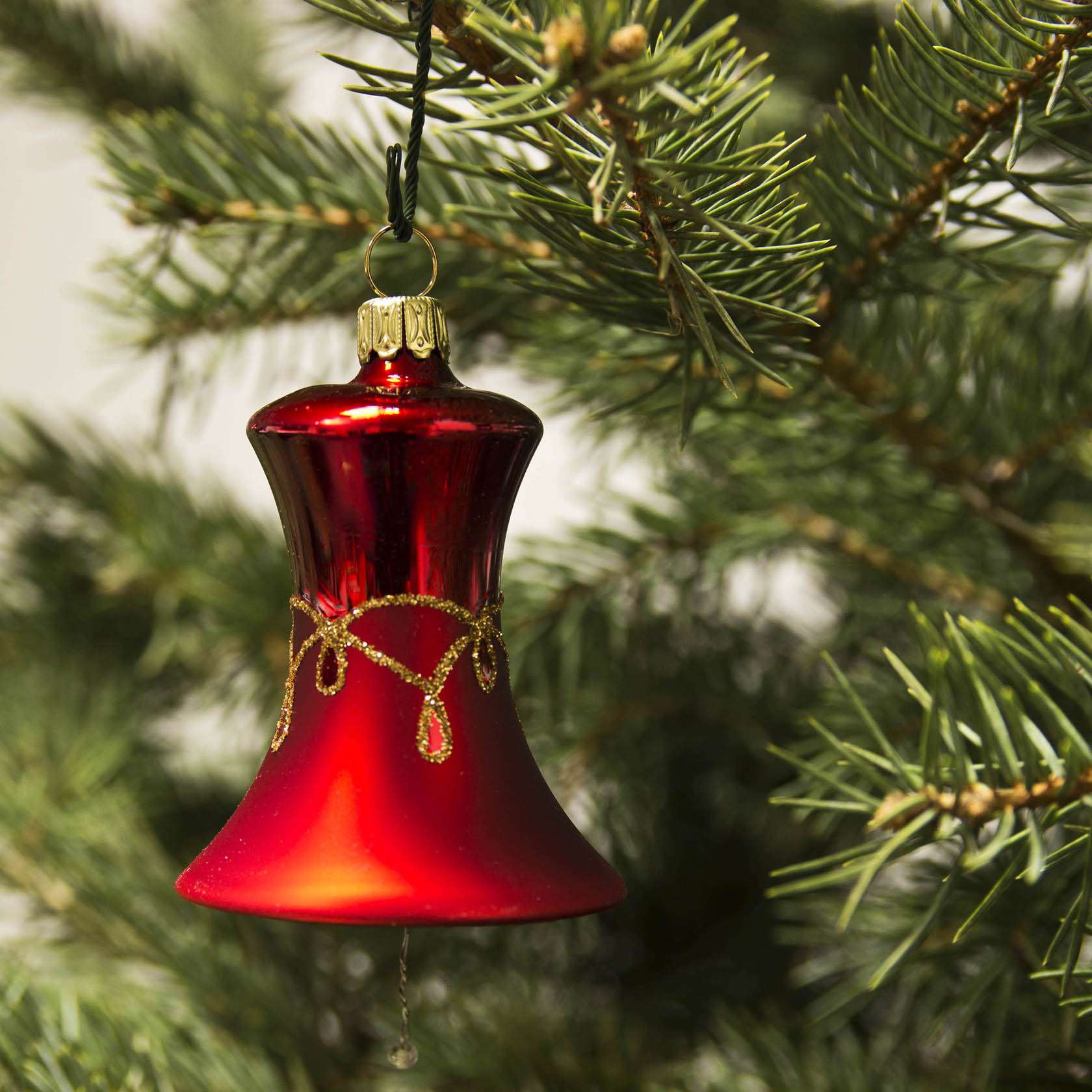Rot-matte Glocke mit goldenem Tropfenmuster als Christbaumschmuck an einem Nadelbaum.