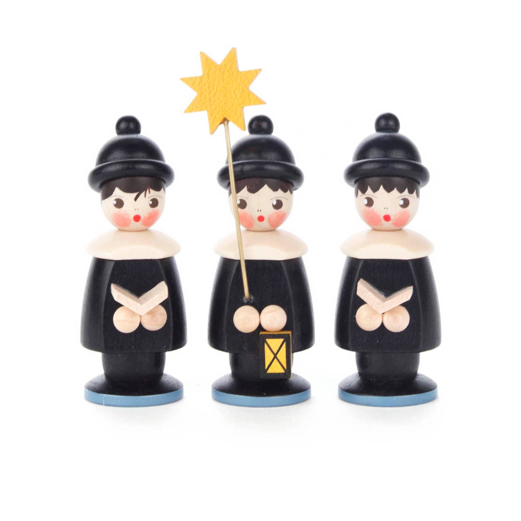 Three black wooden figurines, each with rosy cheeks, wearing a hat and cape. One holds a yellow star on a stick and a lantern.