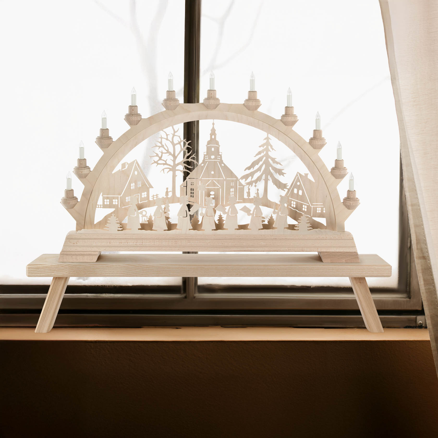 Ein hölzerner Schwibbogen mit Motiven eines Seiffener Dorfs und einer Kurrende, elektrisch beleuchtet, steht auf einem Fensterbrett.