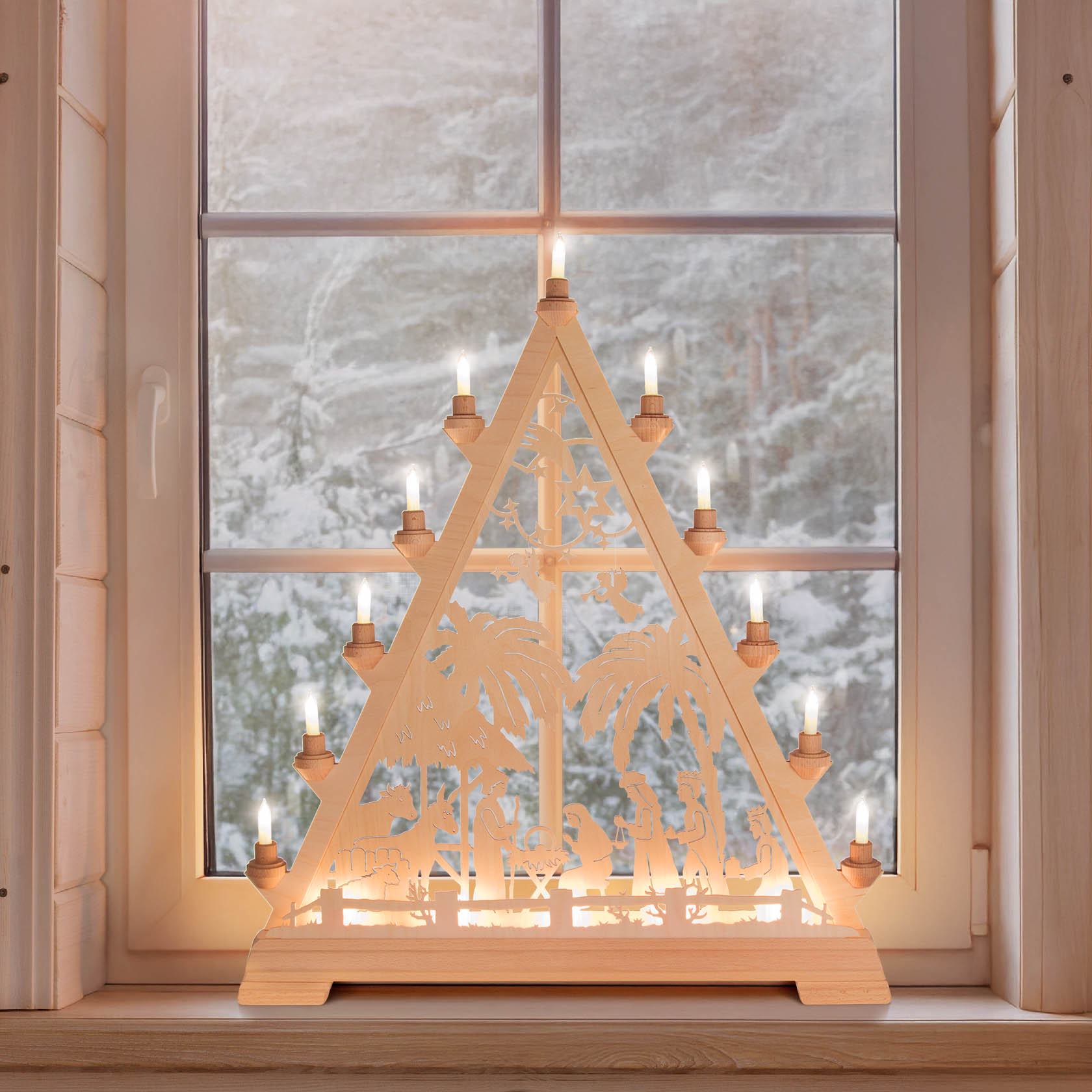 Ein dreieckiger, elektrisch beleuchteter Weihnachtsschmuck auf einem Fensterbrett zeigt die Szene der Geburt Christi mit Figuren wie Maria, Josef und Tieren.