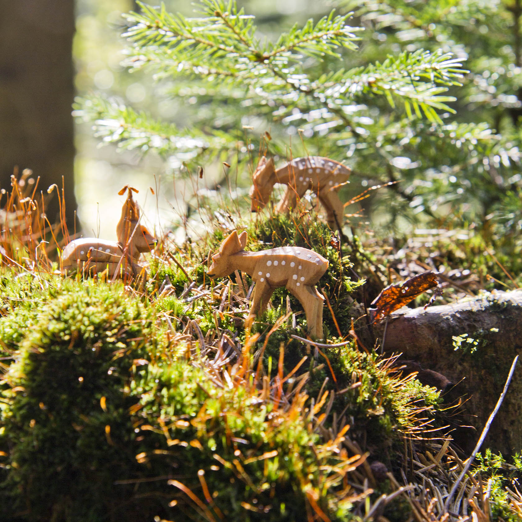 Three intricately carved wooden fawn figurines, positioned as if they are grazing on a mossy forest floor.