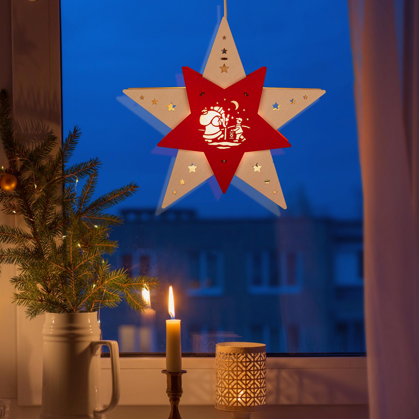 Ein LED-Fensterstern in Weiß und Rot mit einer Abbildung von Knecht Ruprecht, beleuchtet im Dunkeln vor einem Fenster mit Kerze und Tannenzweig.