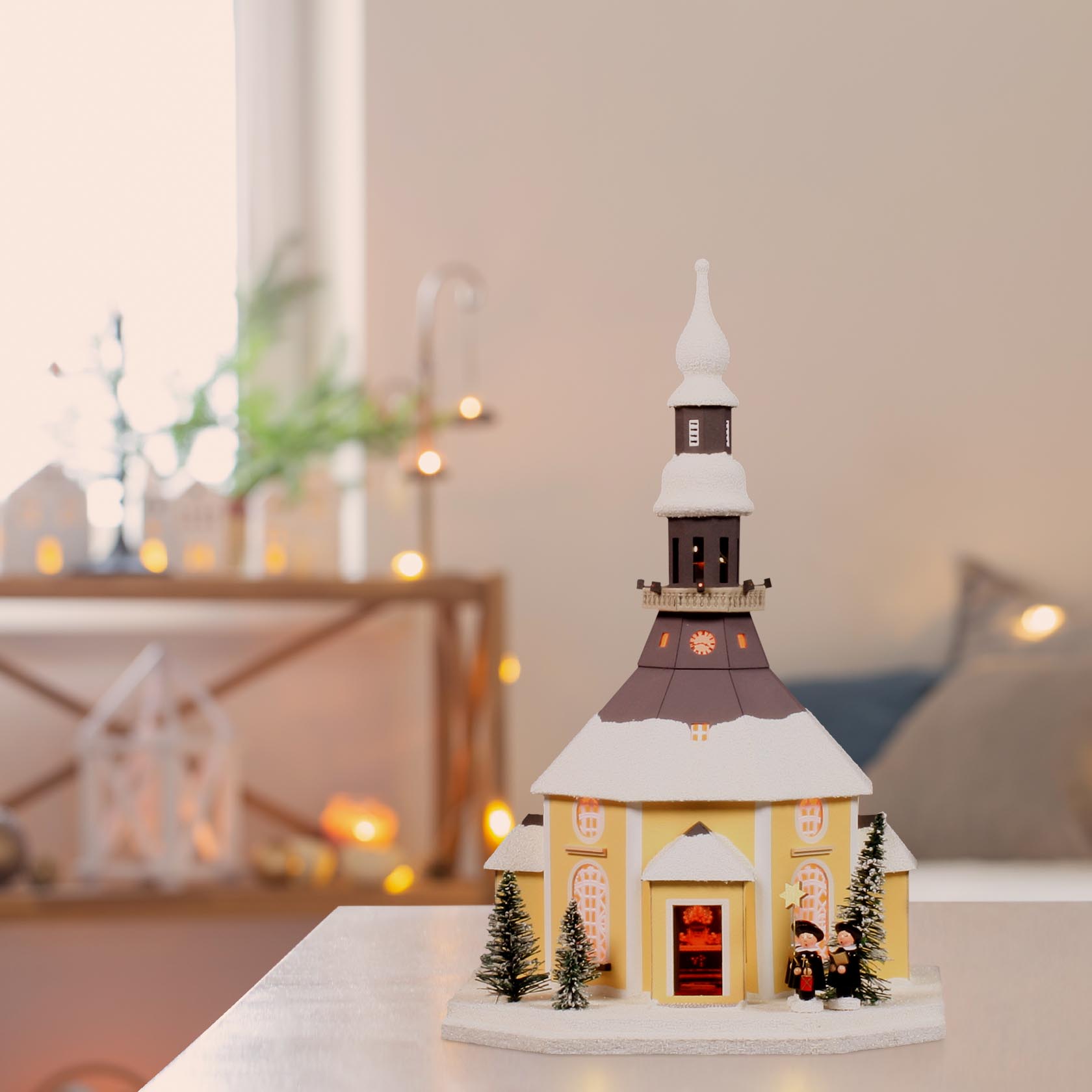 Ein Lichterhaus in Form der Seiffener Kirche mit einer Gruppe von Kurrendesängern davor. Das Gebäude ist schneebedeckt und elektrisch beleuchtet.