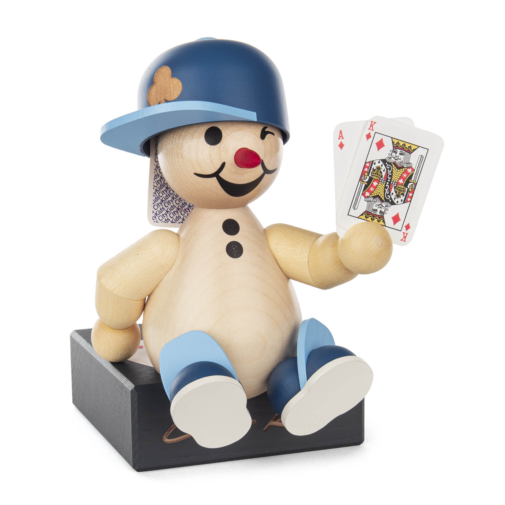 Holzfigur eines lächelnden Kindes mit blauer Mütze, das auf einem schwarzen Block sitzt und ein Kartenspielambon hält, wobei der König sichtbar ist. im Dregeno Online Shop günstig kaufen