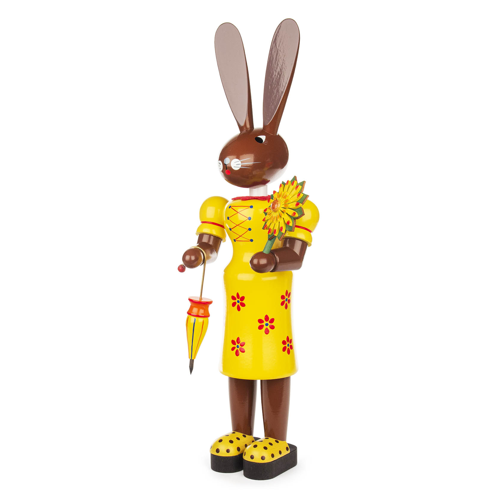 Holzfigur einer Hasenfrau in gelbem Kleid mit roten Blumenmustern und gelben Schuhen. Sie hält einen gelben Schirm und eine Sonnenblume in der Hand.