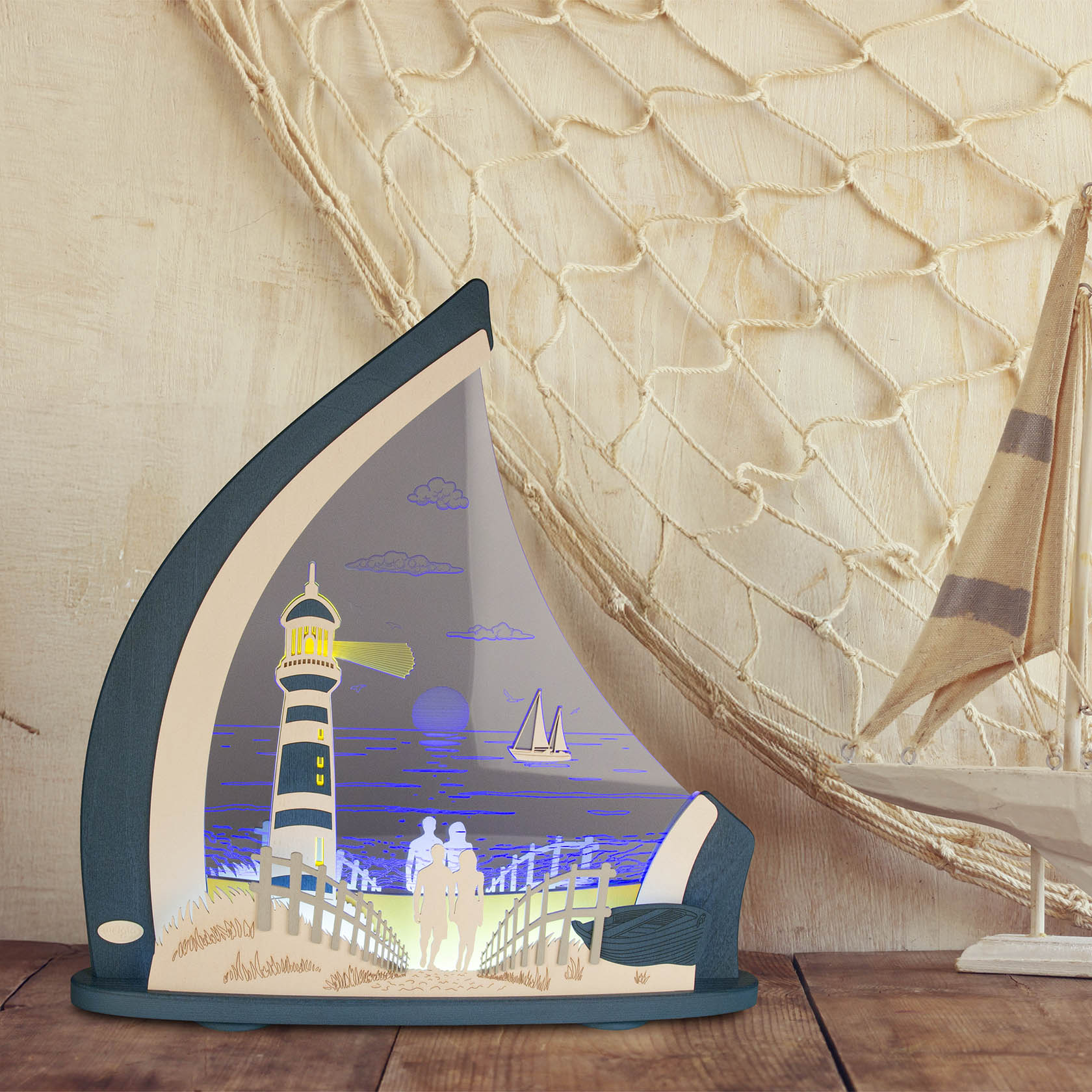 Eine LED-Lichterspitze mit maritimem Motiv: Ein Leuchtturm, ein Segelboot, ein Paar am Strand und eine Netzdekoration im Hintergrund.