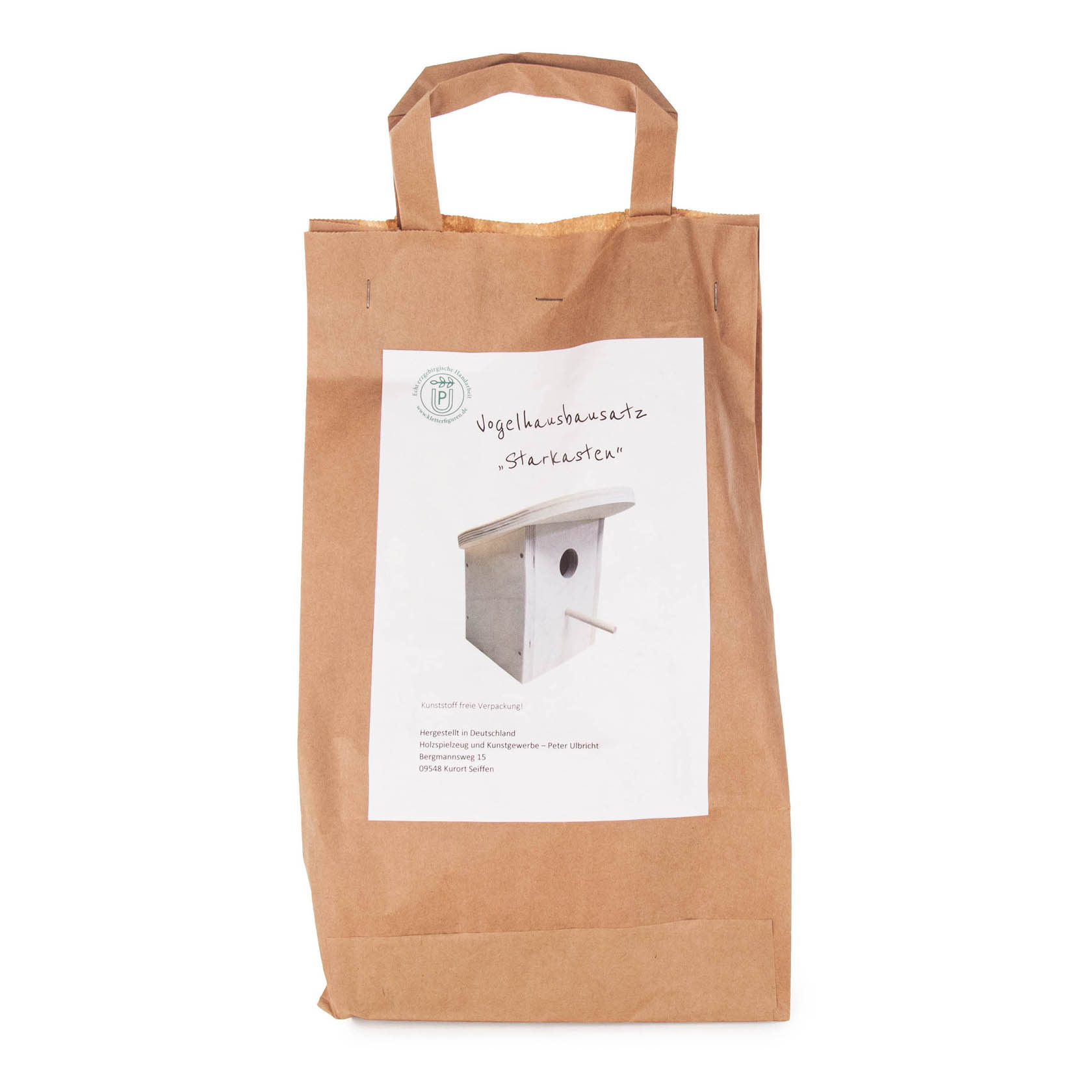 A brown paper bag containing a birdhouse kit labeled 'Starkasten'. The label shows an image of the assembled wooden birdhouse.