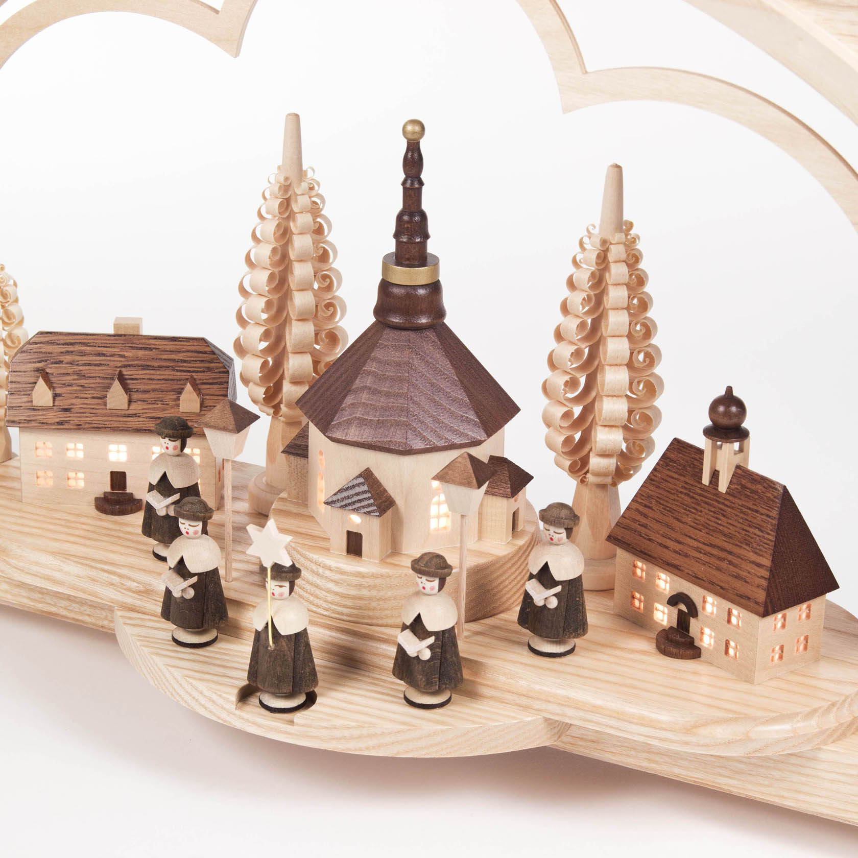 Wooden arch with illuminated Seiffen village scene featuring a church and choir figures, accompanied by two spiral trees and small houses.
