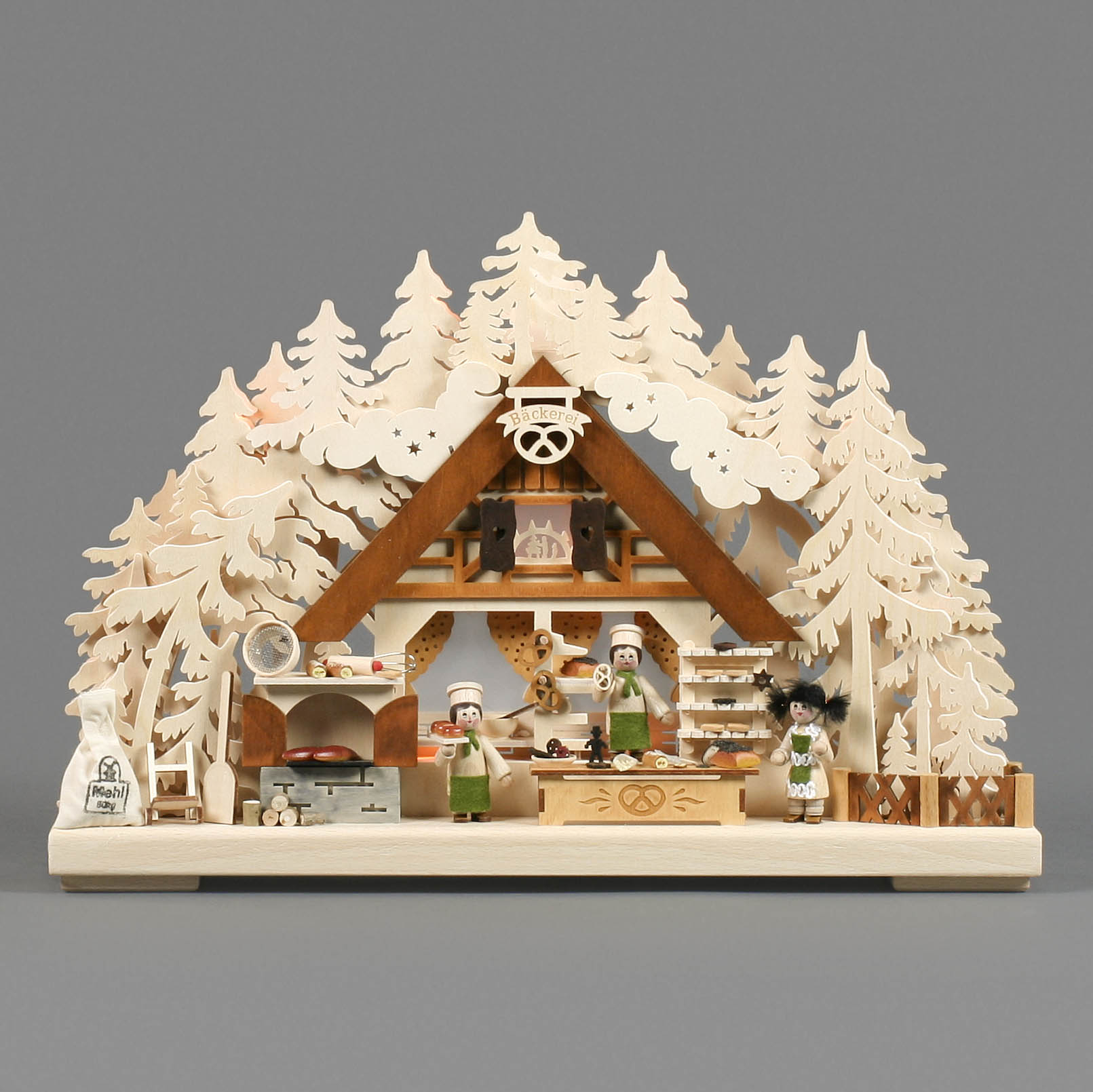 An intricately designed miniature landscape featuring a bakery scene with two bakers, a decorative arch, and house surrounded by carved trees.