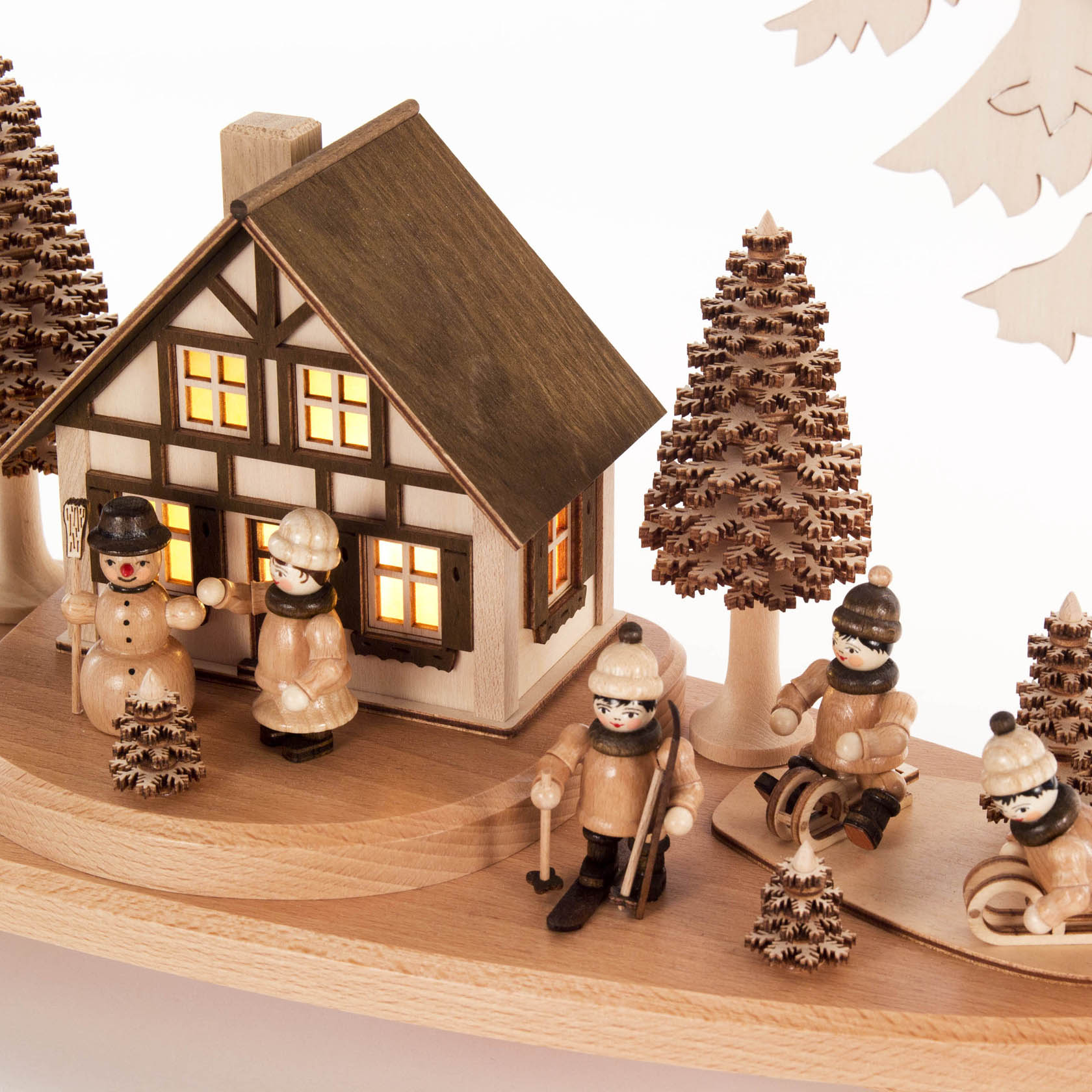 Ein Schwibbogen mit einem beleuchteten Haus, umgeben von Winterkindern-Figuren, die Skier tragen und Schlitten fahren, sowie dekorativen Bäumen.