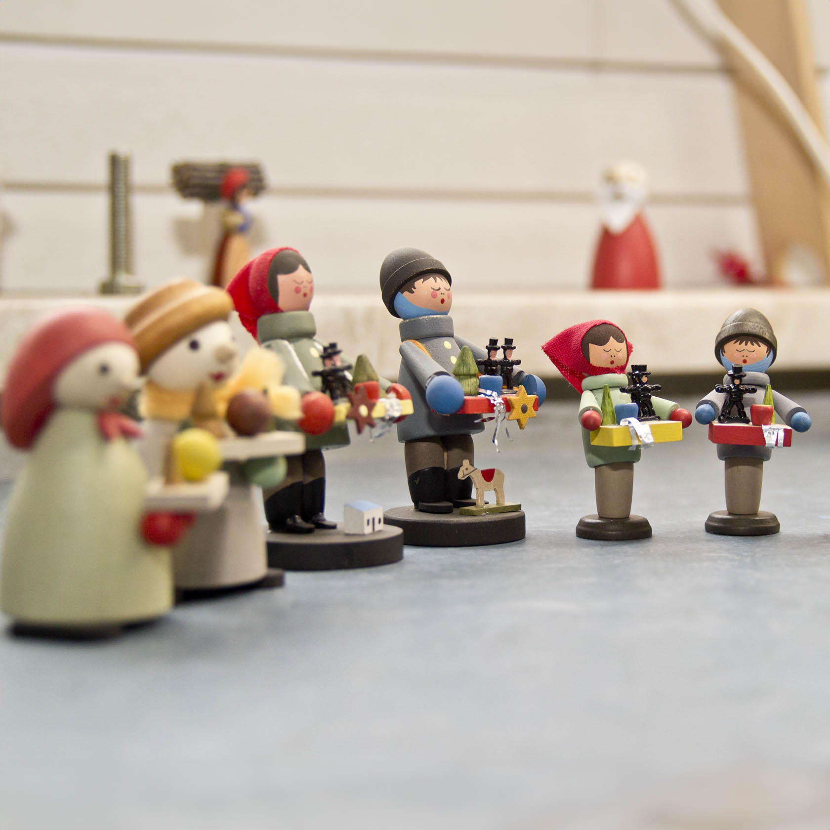 Figurines of children holding candles and gifts, dressed in winter attire with scarves and hats. Three figures are standing closer, while two are slightly apart.