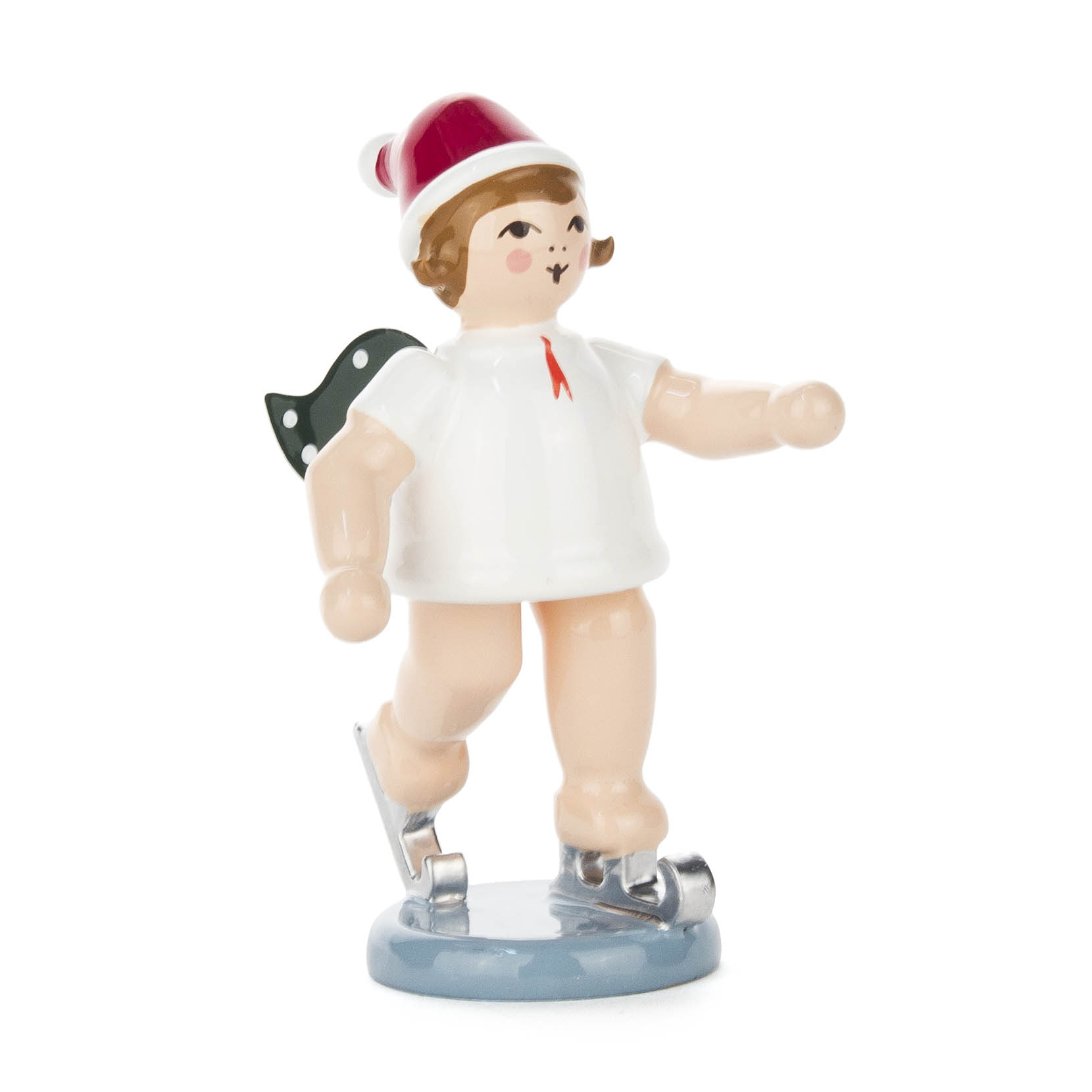 Eine Engel-Figur mit Mütze und grünen Flügeln auf Schlittschuhen, steht auf einem blauen Sockel, in Bewegung angedeutet.