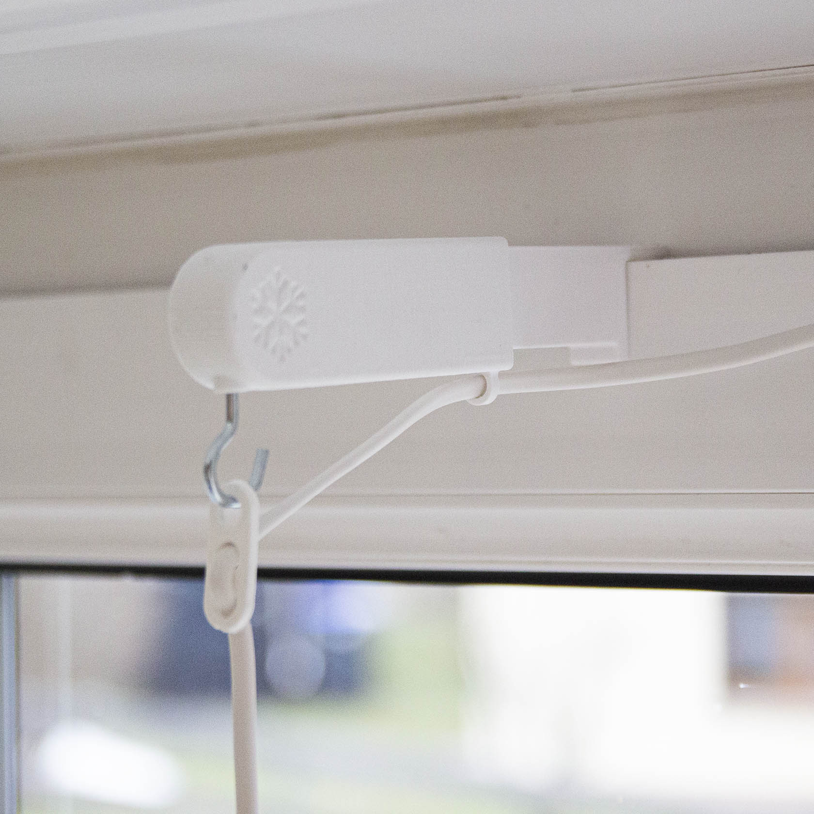 Weiße Stern- und Laternenhalterung mit verstellbarer Kabelführung an einem Fensterrahmen angebracht.