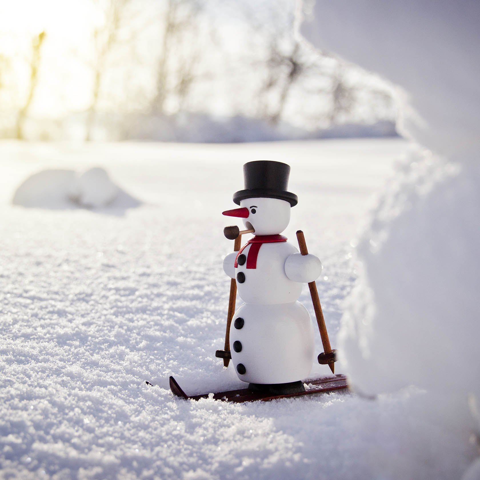 Ein Schneemann als Räuchermann auf Skiern mit rotem Schal und schwarzem Hut steht im Schnee.