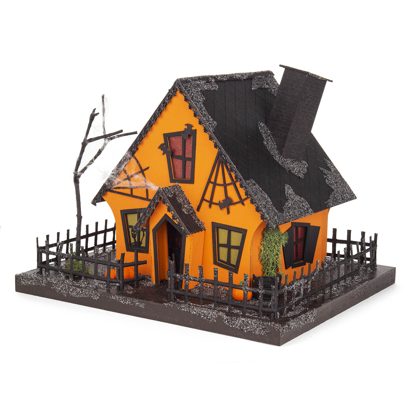 Dekoratives Kürbishaus mit schwarzem Dach, schiefen Fenstern in verschiedenen Farben, Schornstein und Zaun. Perfekt für Halloween-Dekor.