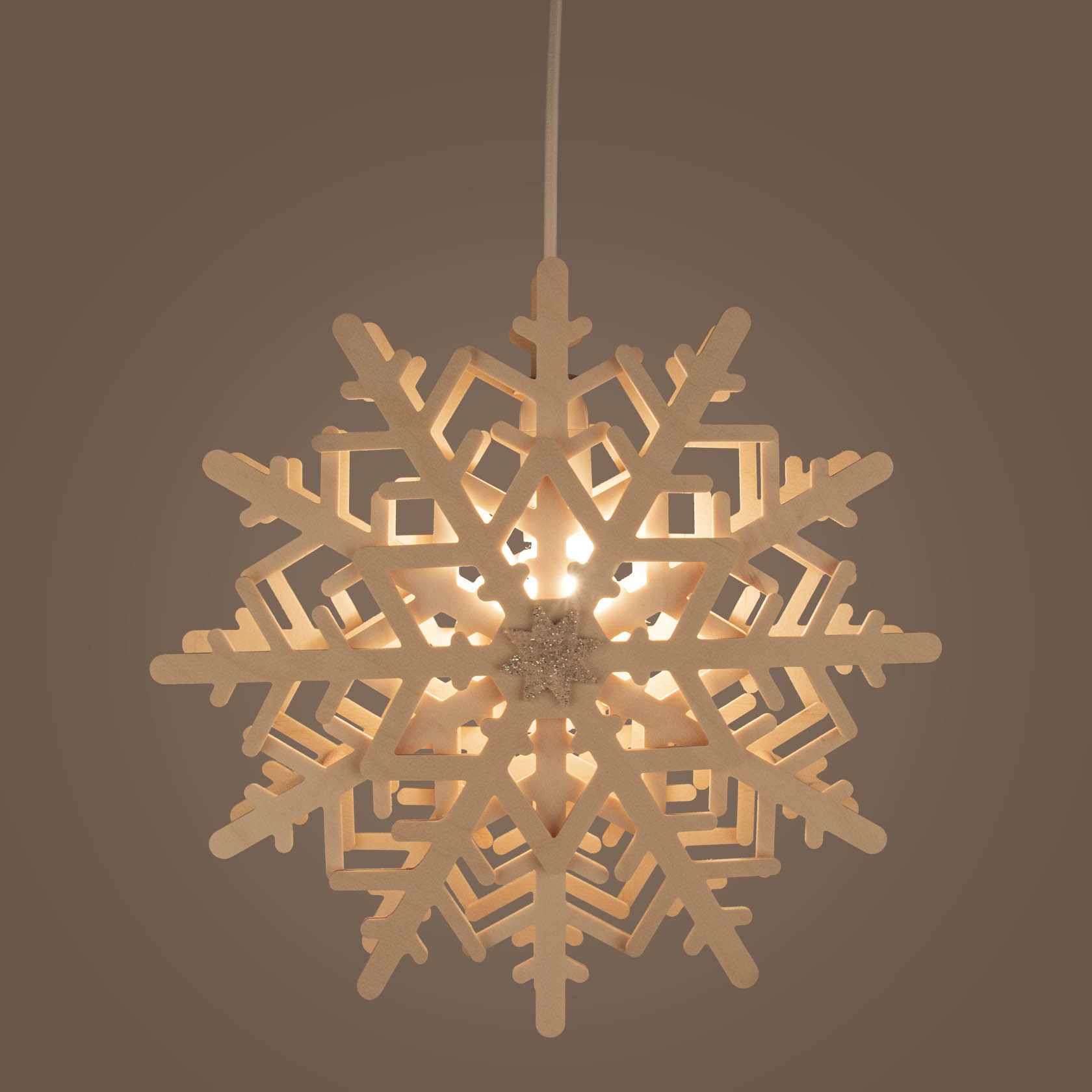 A lit snowflake window decoration with intricate symmetrical patterns glowing with warm electric light.