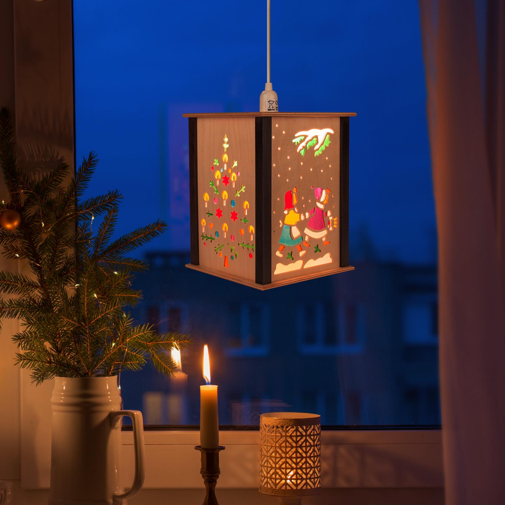 A lantern with children's motifs is hanging from the ceiling. It depicts children playing in the snow near a decorated Christmas tree.