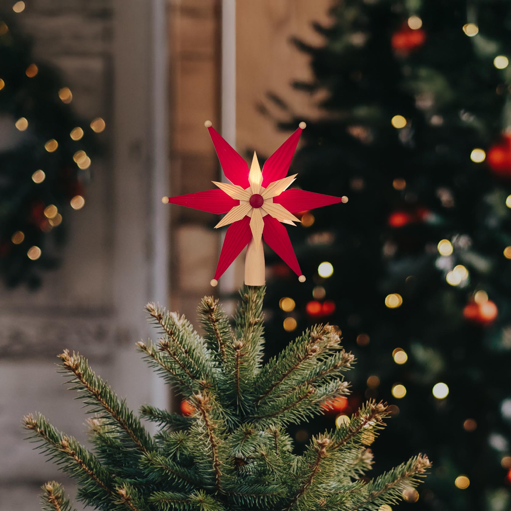 Rote und naturfarbene Christbaumspitze mit elektrischer Beleuchtung, die auf einem Weihnachtsbaum angebracht ist.