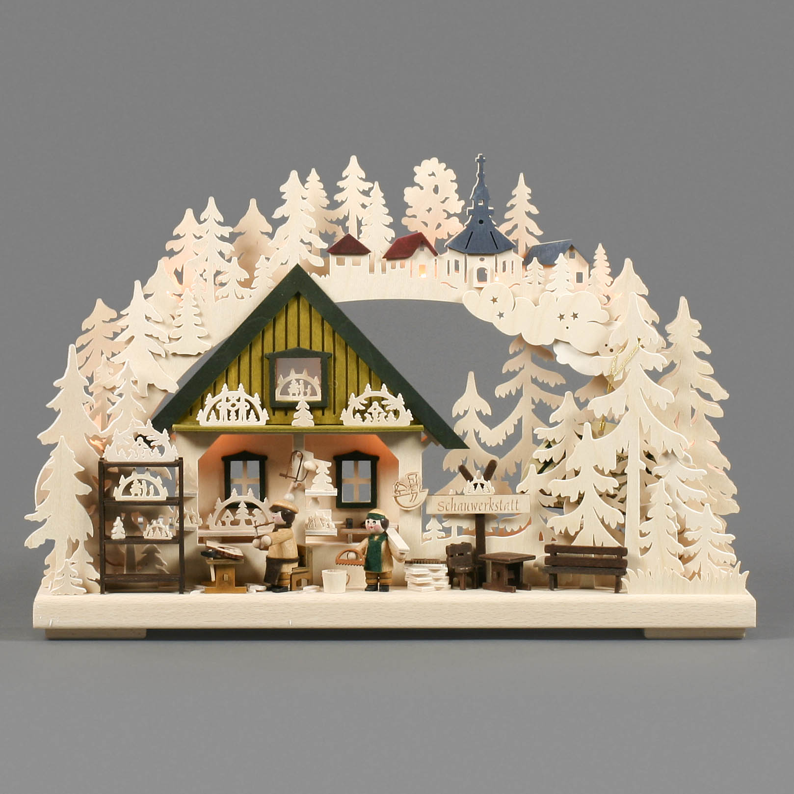 Illuminated Schwibbogen depicting a workshop scene with craftsmen creating Schwibbogen under a decorated wooden arch with trees and houses.
