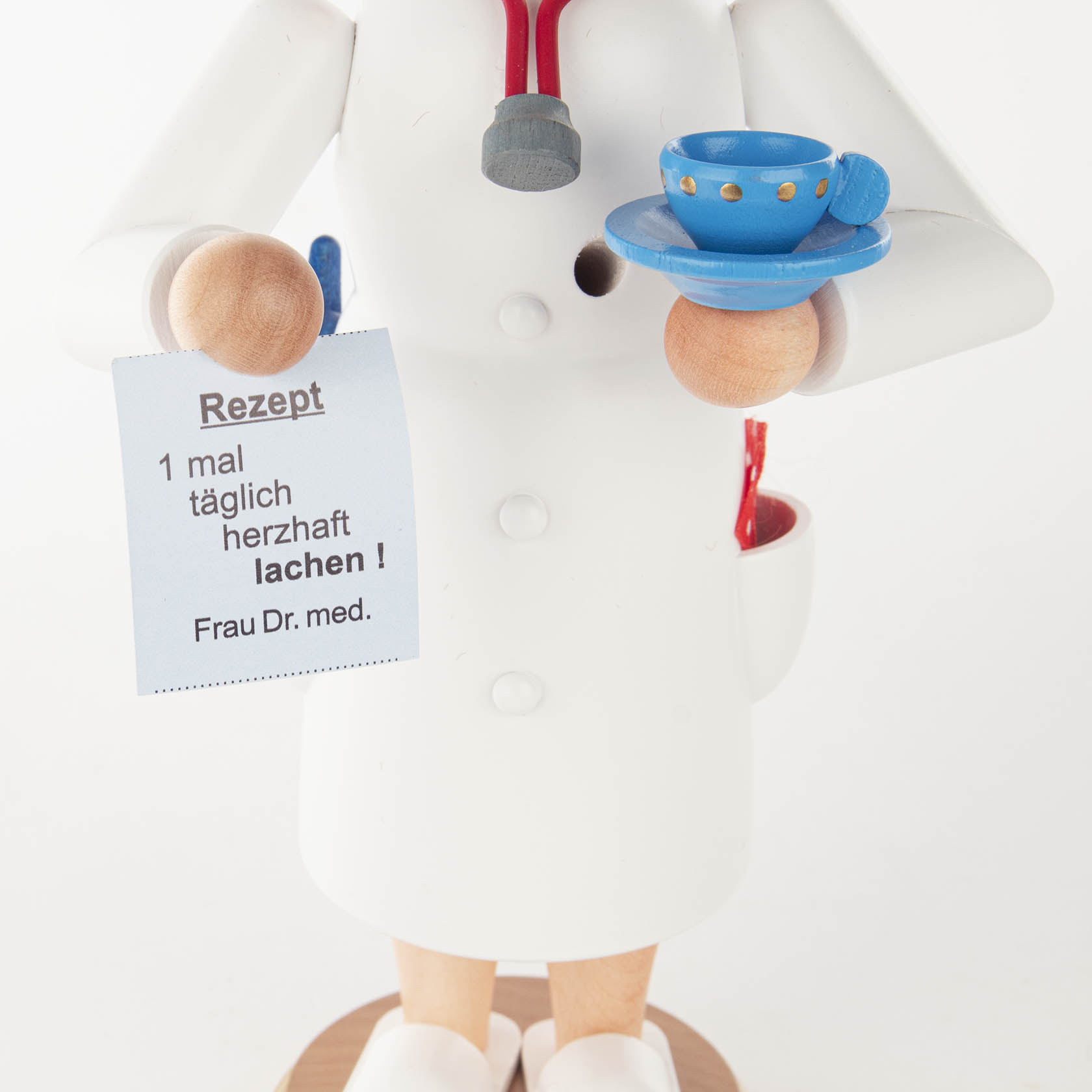 Räucherfigur einer Ärztin mit braunen Haaren, die ein Rezept in der einen Hand und eine blaue Tasse in der anderen hält. Das Rezept sagt: '1 mal täglich herzhaft lachen!'.